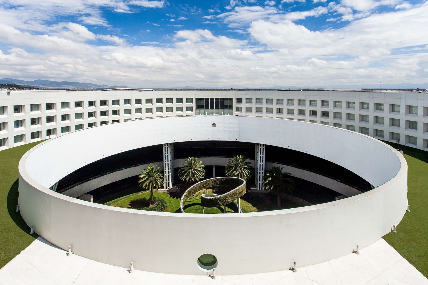 Modern circular building with white exterior and courtyard garden viewed from multiple angles against blue sky.
