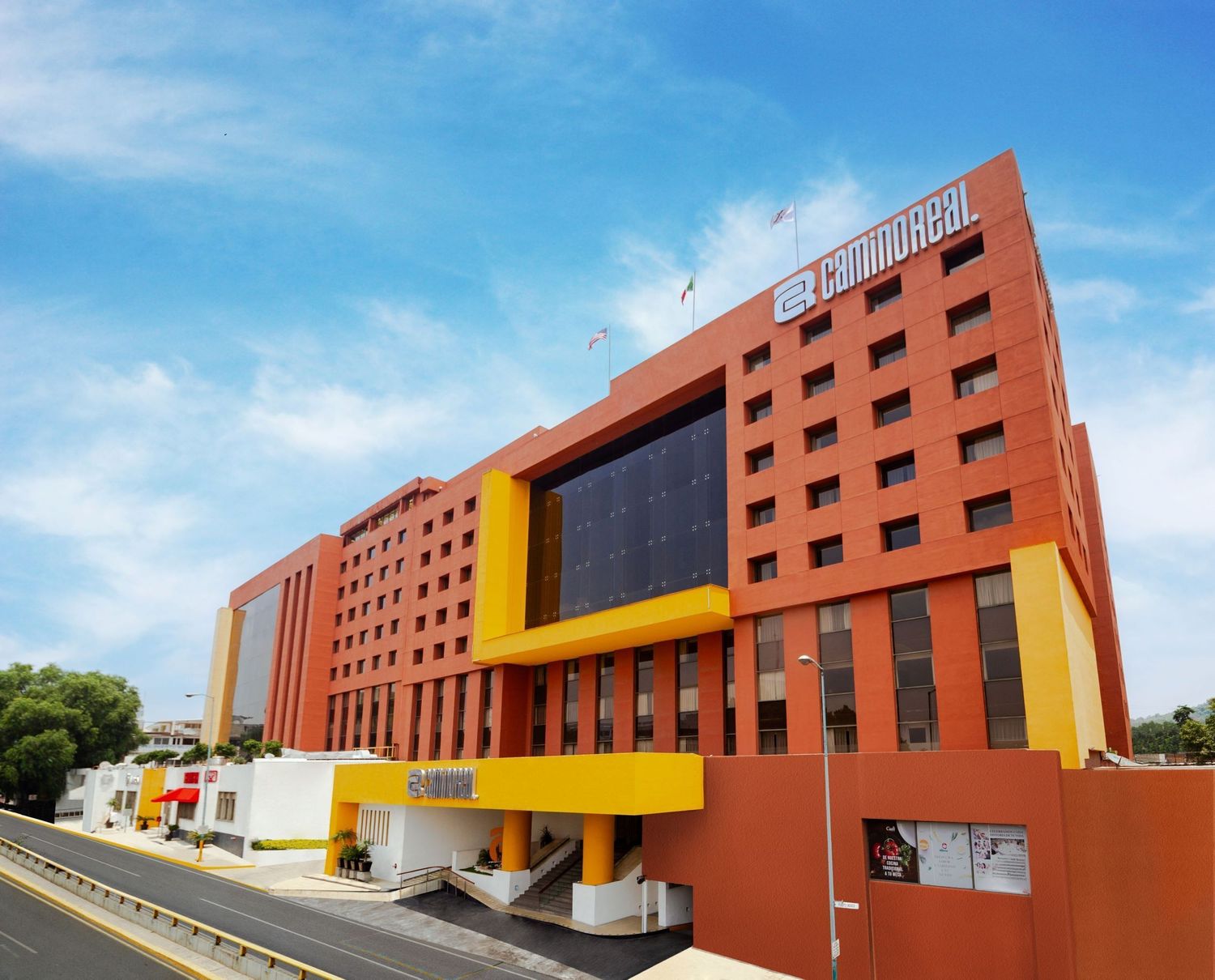 Modern terracotta-colored building complex with yellow architectural accents against a bright blue sky.