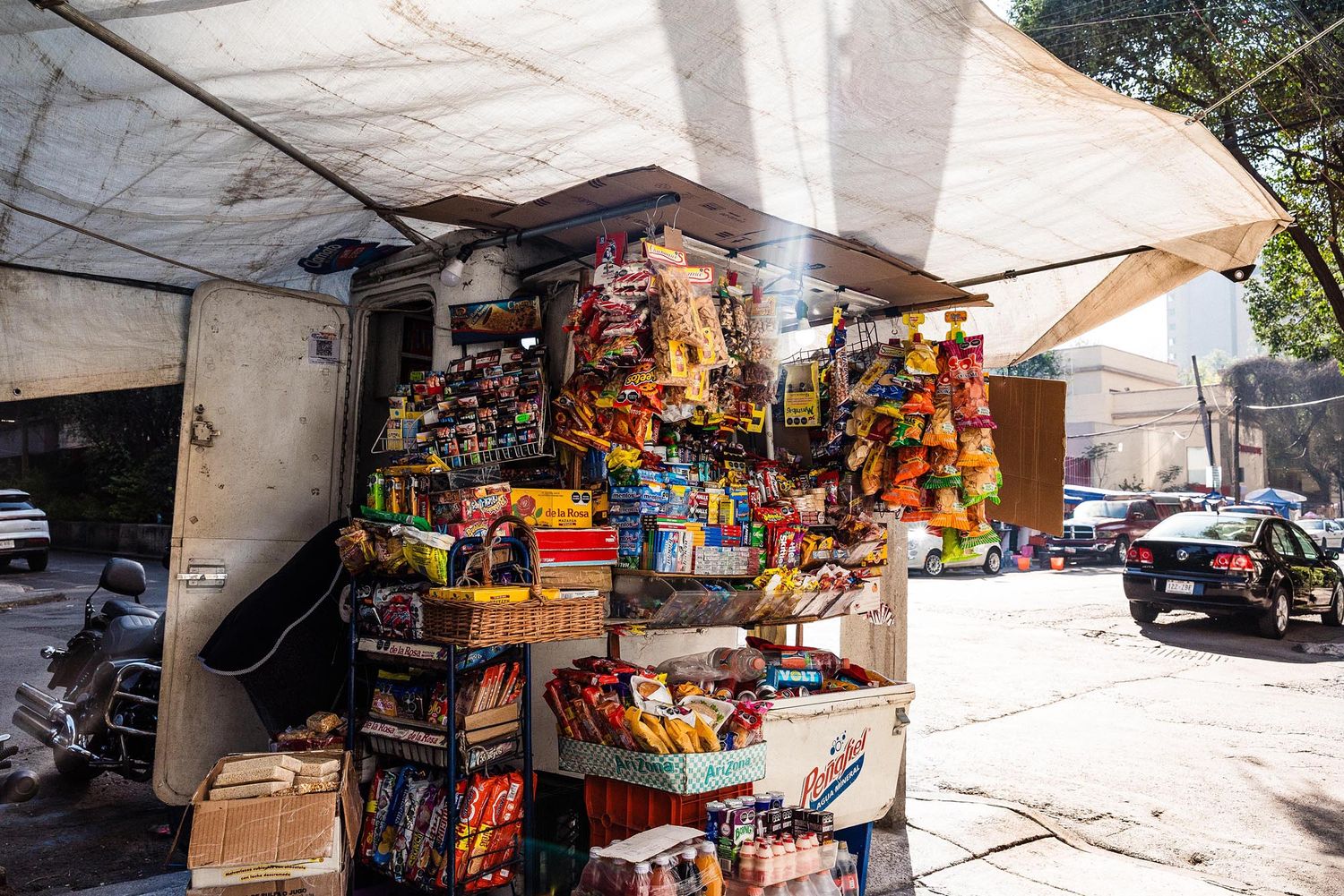 Colorful snack and candy vendor stand on city street with awning displaying various packaged goods for sale.