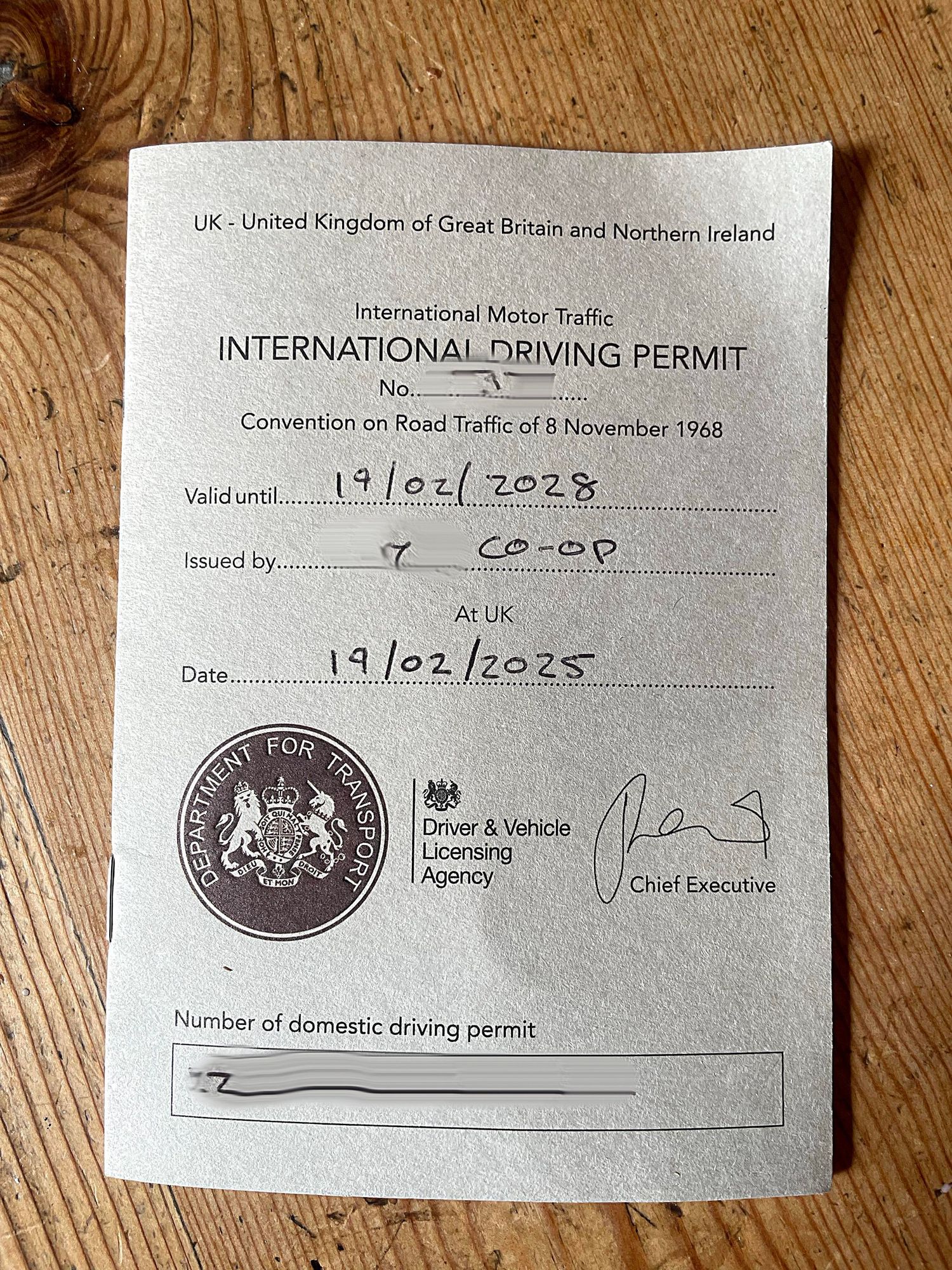 UK international driving permit document showing expiry date and official seal on wooden surface.