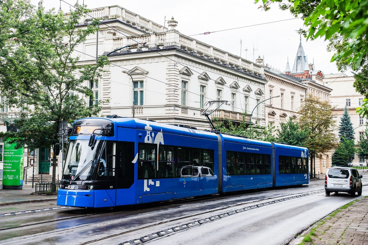 A modern blue tram travels along tracks in front of a historic building in Krakow, Poland.