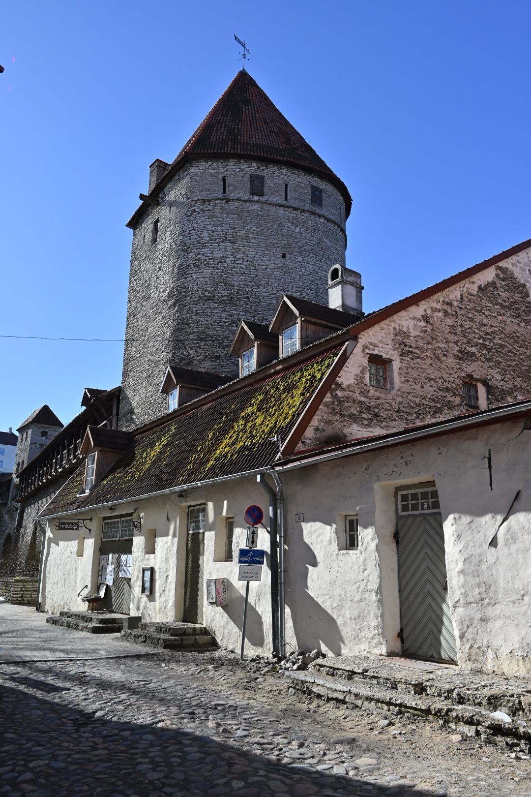 Ancient watchtower rises above white-washed buildings along cobblestone street in medieval town.