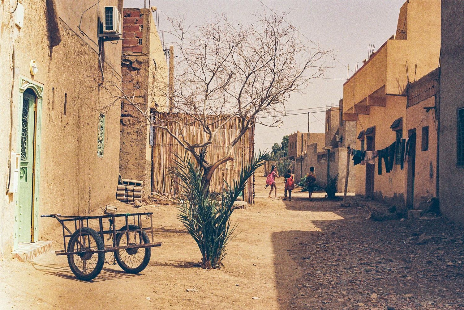 Panoramic view of an empty desert town street with adobe buildings and bare trees against a cloudy sky.