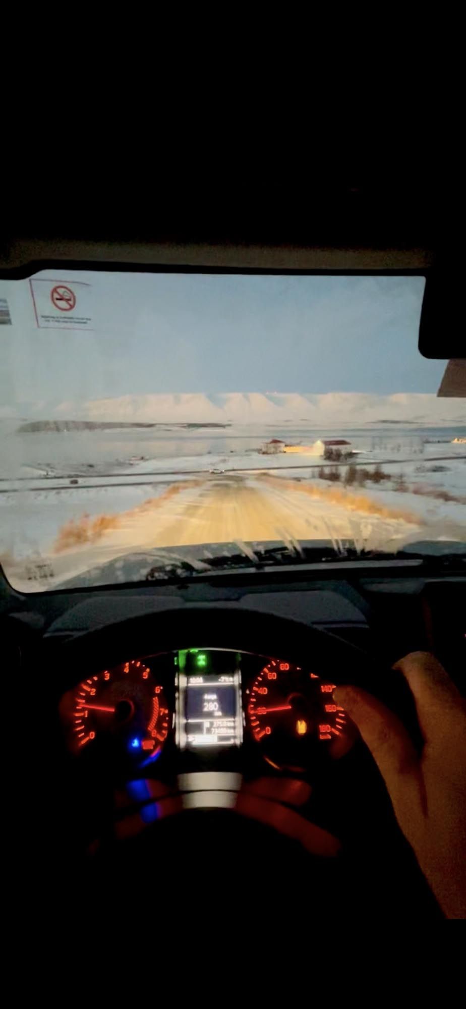 View through car windshield of snowy winter road with illuminated dashboard gauges showing speed and fuel levels.