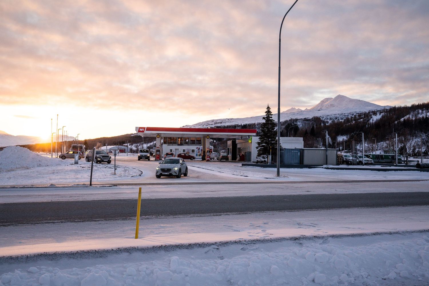 Snow-covered gas station with mountains in the background during a colorful arctic sunset.