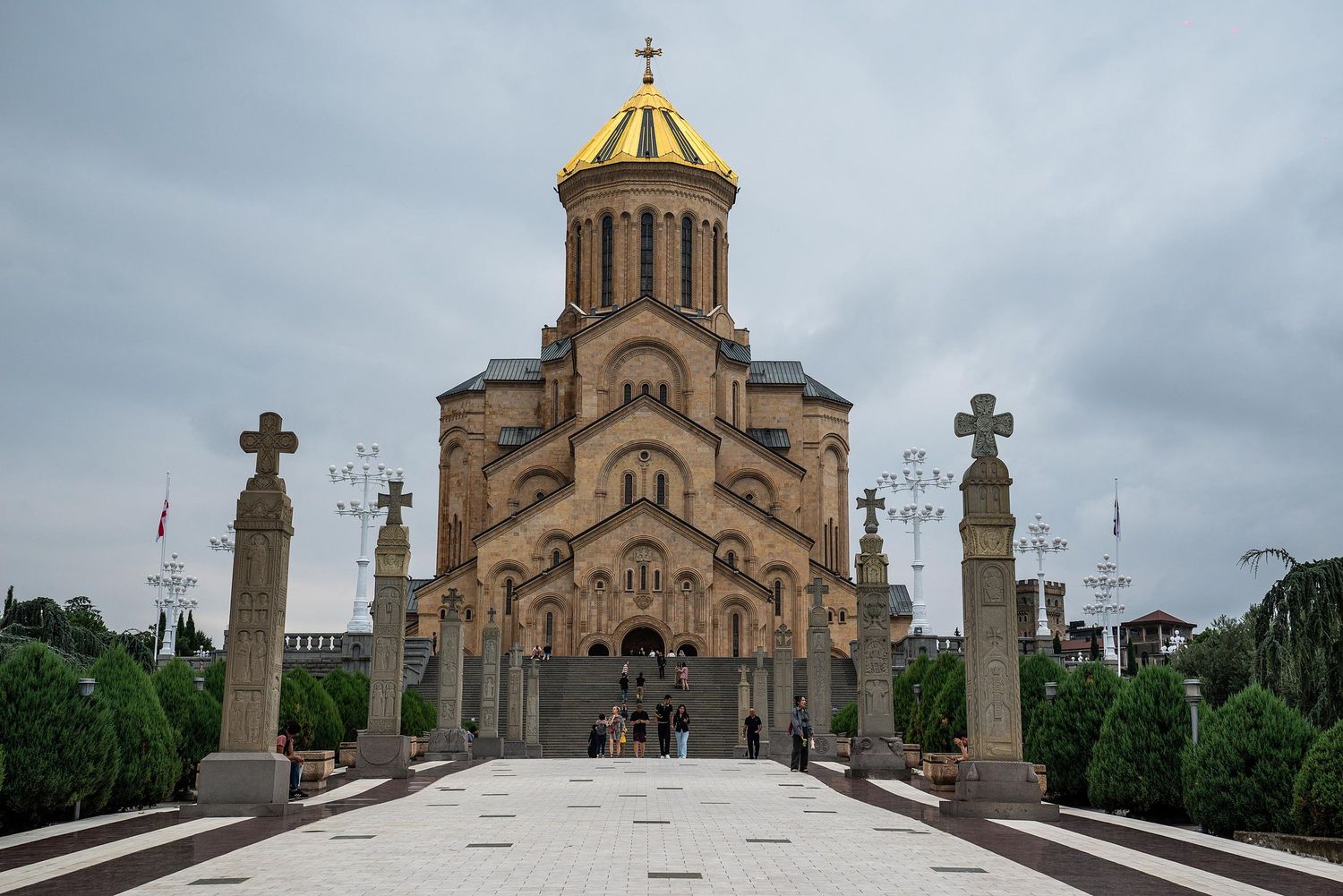 Holy Trinity Cathedral in Tbilisi features golden domes and crosses against a cloudy sky.