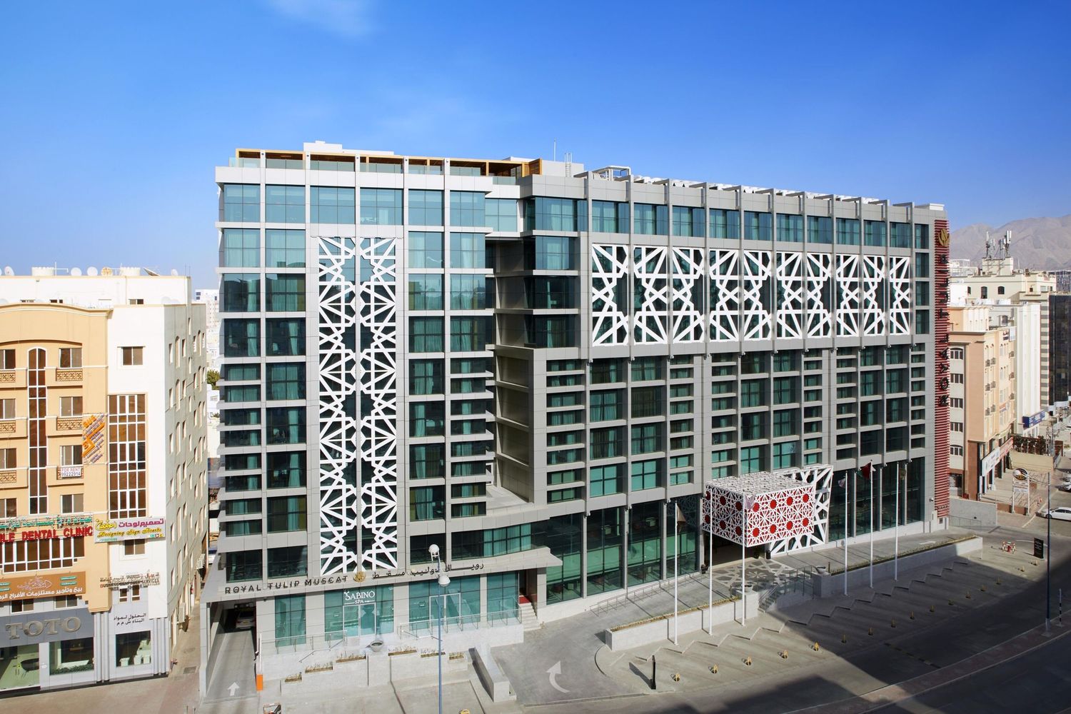 Modern office building facade with geometric patterns and glass windows stretches along a sunny urban street.