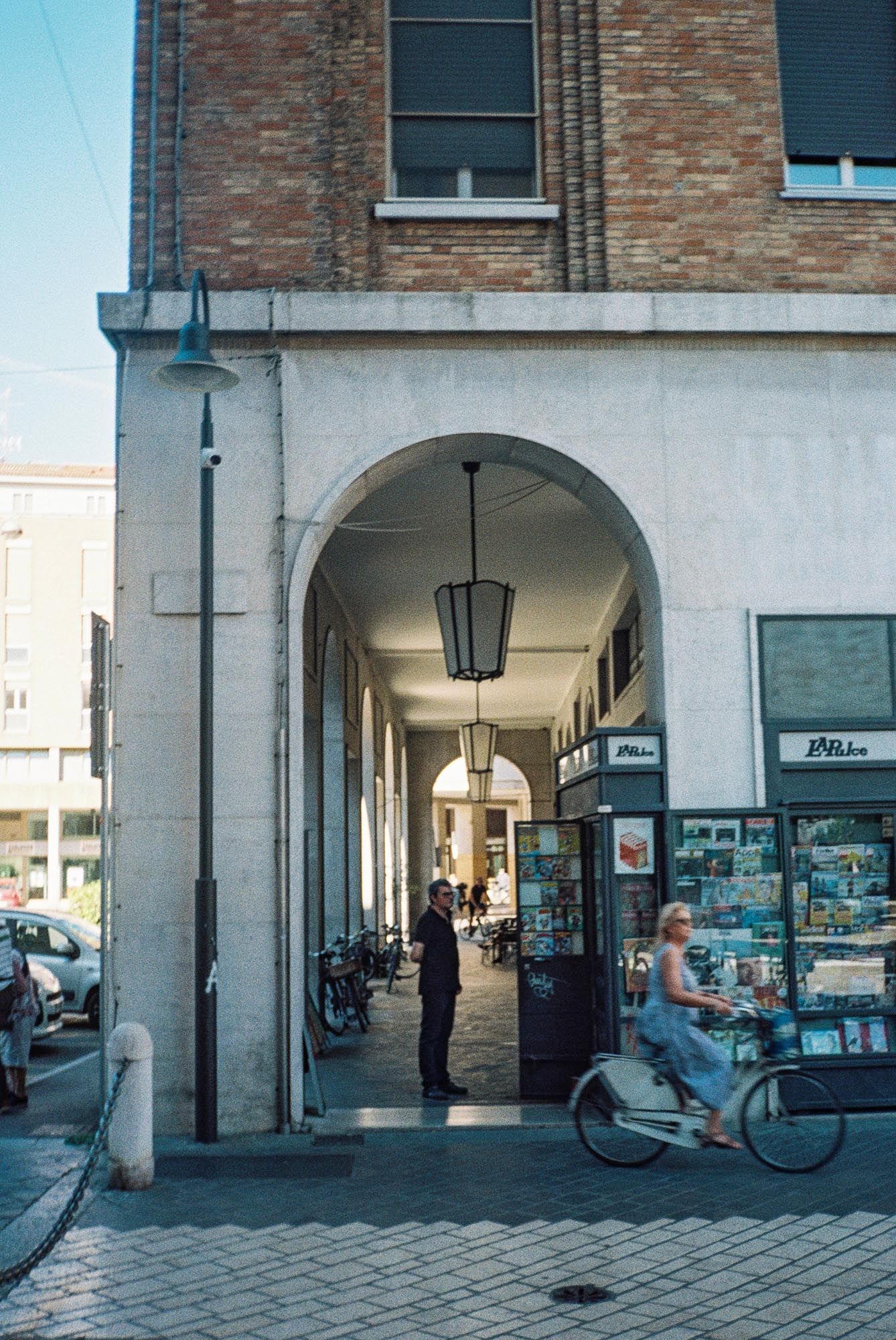 A covered archway entrance with brick building facade, parked bicycles and street lamp in an Italian shopping district.