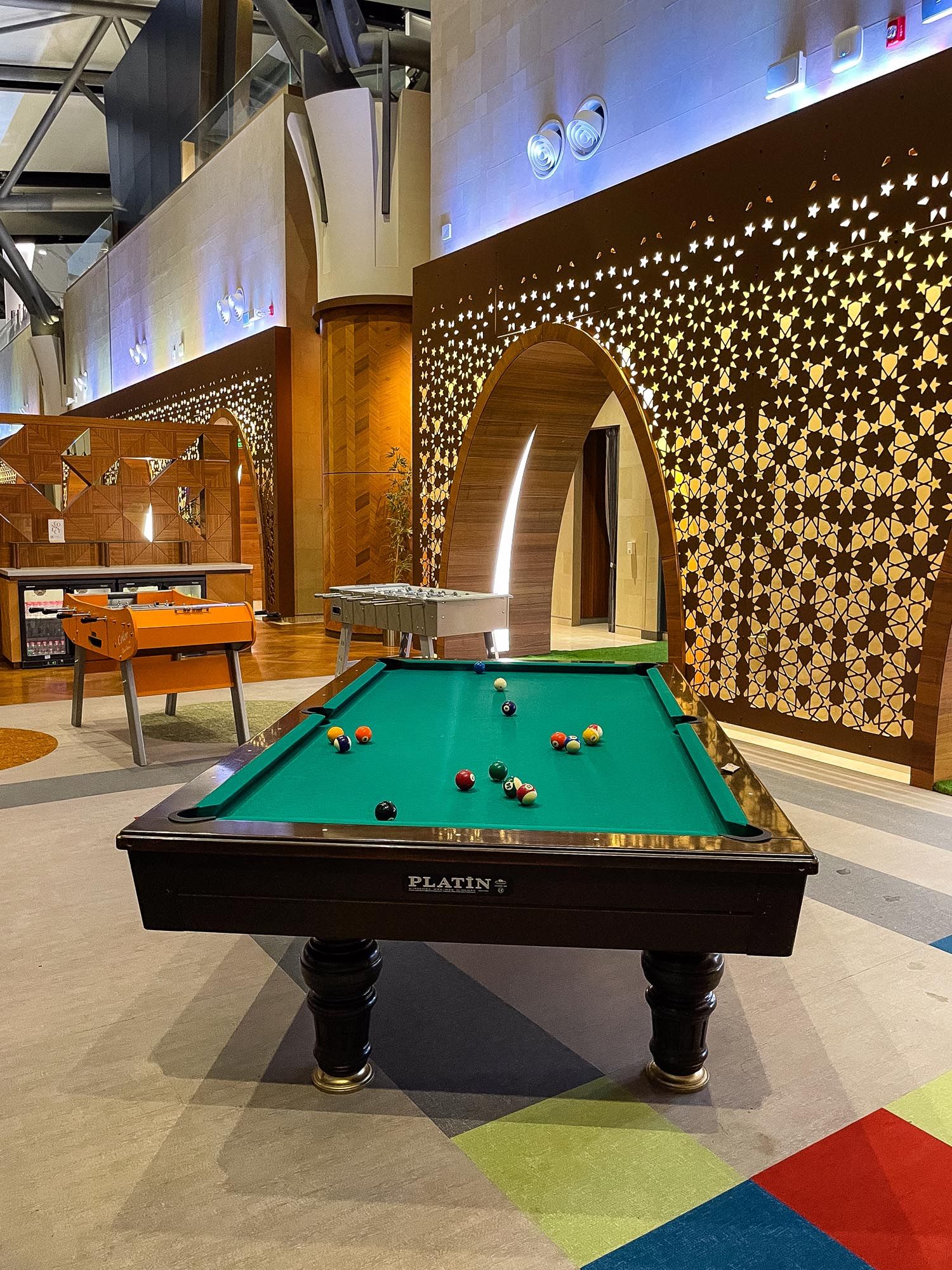 Six connected pool tables arranged in a modern game room with illuminated star-patterned wall decorations.