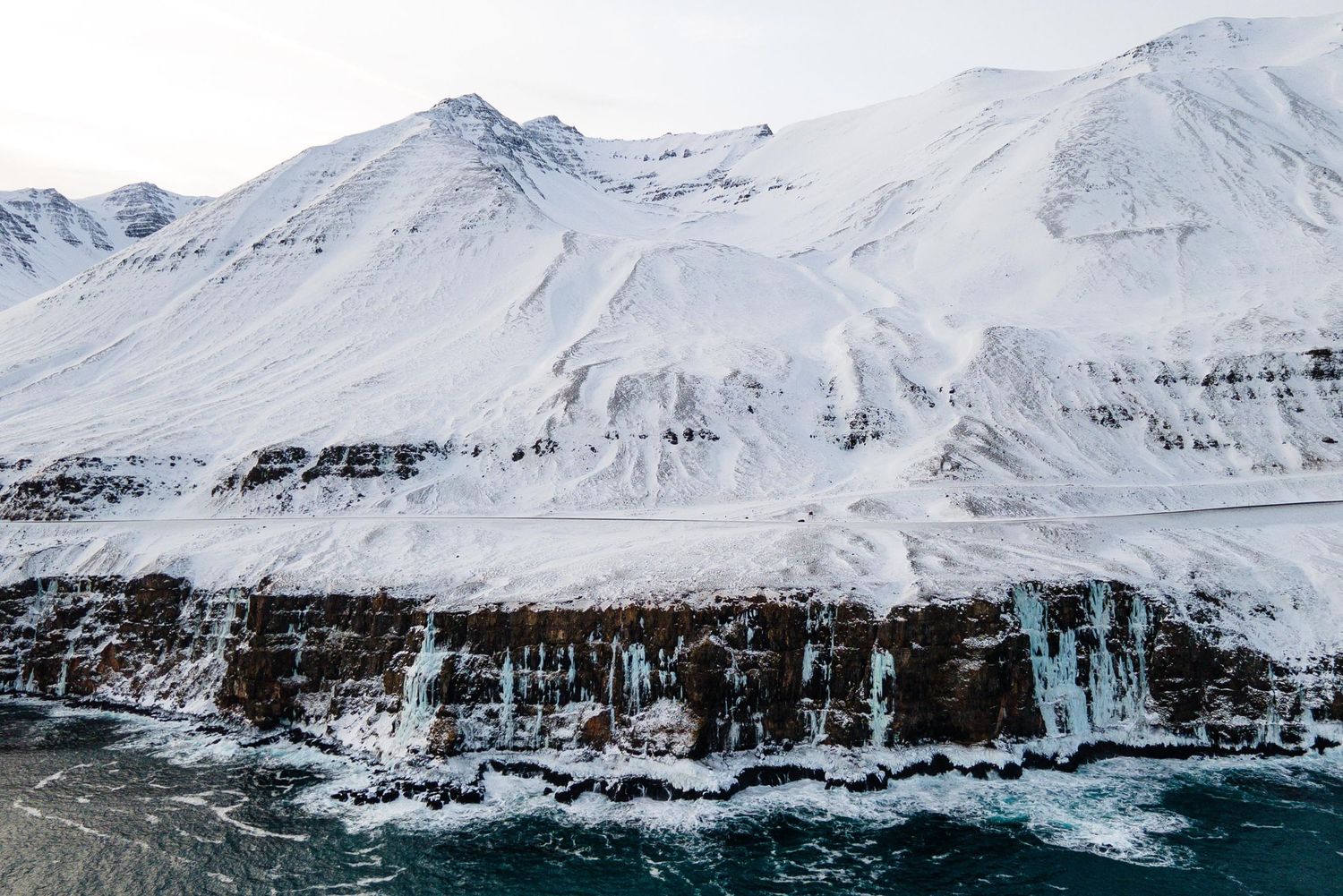 Snow-capped mountains rise above a dramatic glacial coastline in the Arctic wilderness during winter.