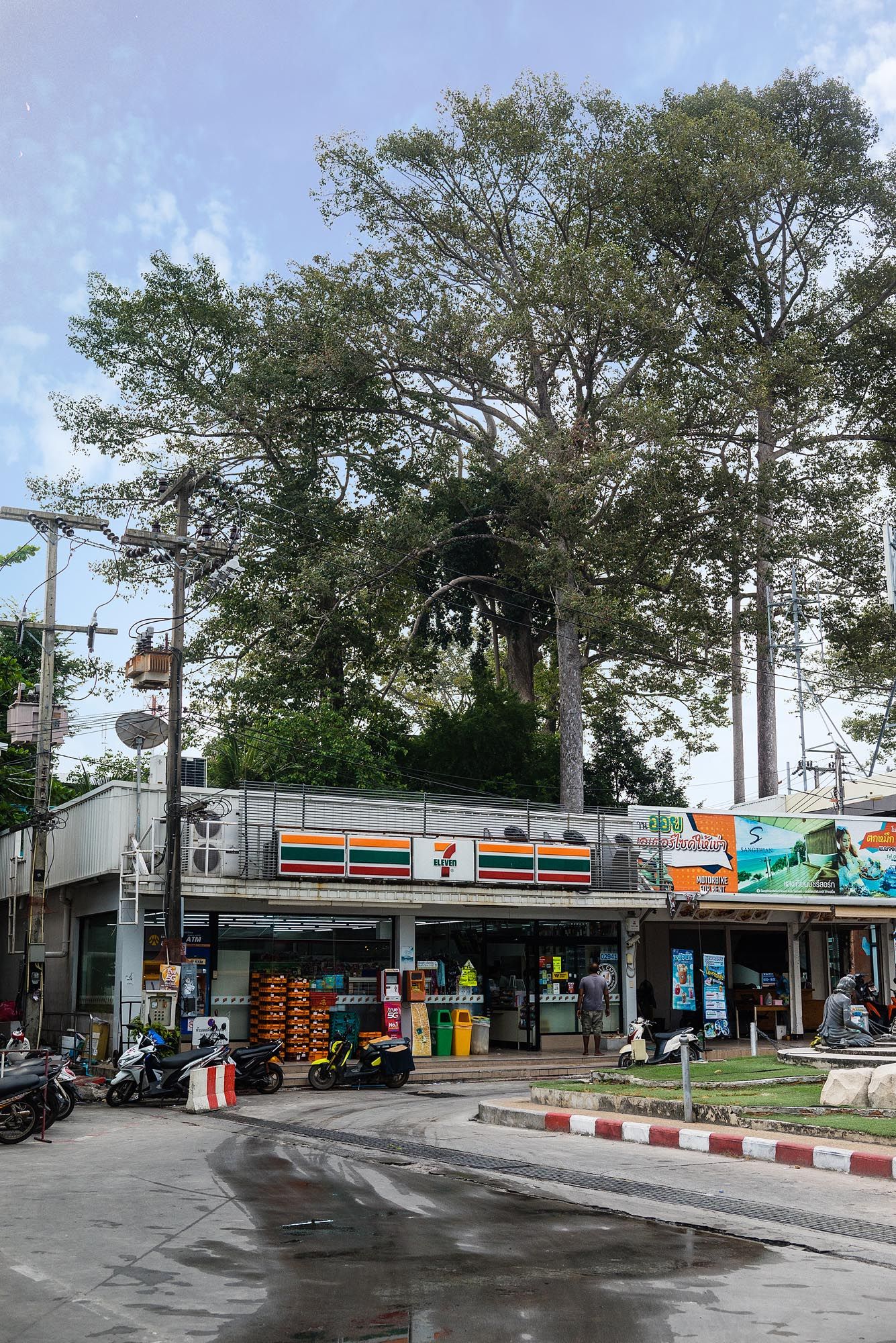 A 7-Eleven convenience store exterior with parking lot and trees visible in multiple connected storefront views.