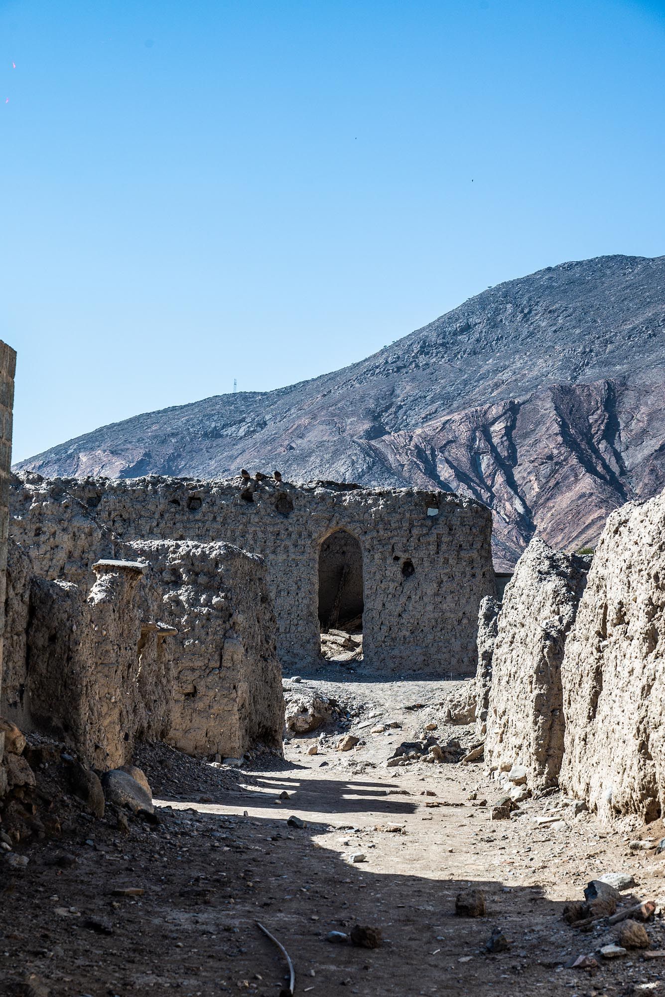 Ancient stone ruins and walls line a path through rugged mountain terrain under clear blue skies.