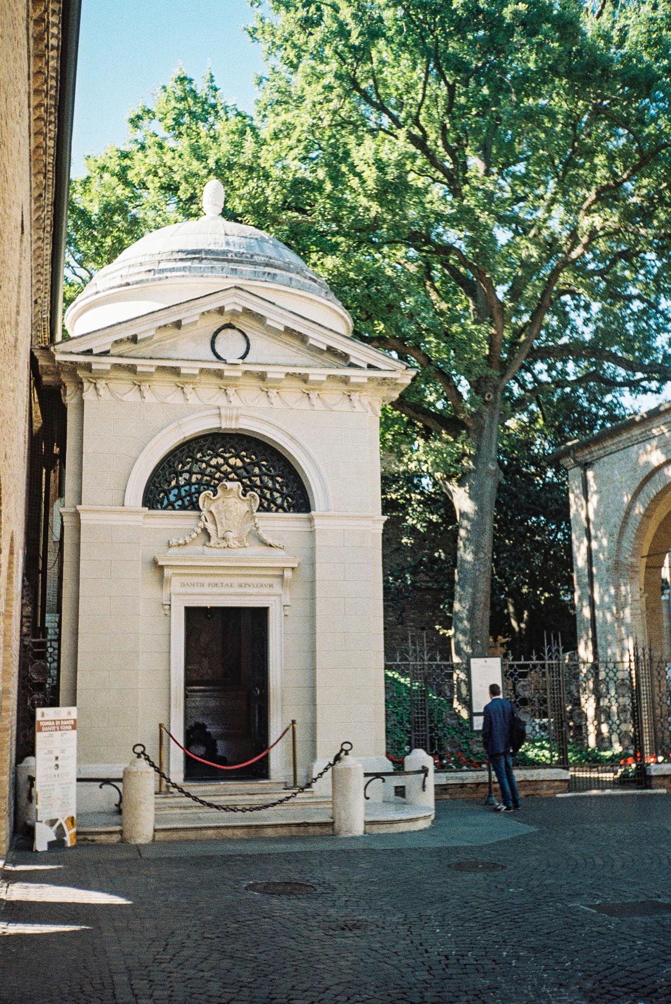 White stone mausoleums with classical architecture line a shaded cemetery path in Pere Lachaise, Paris.
