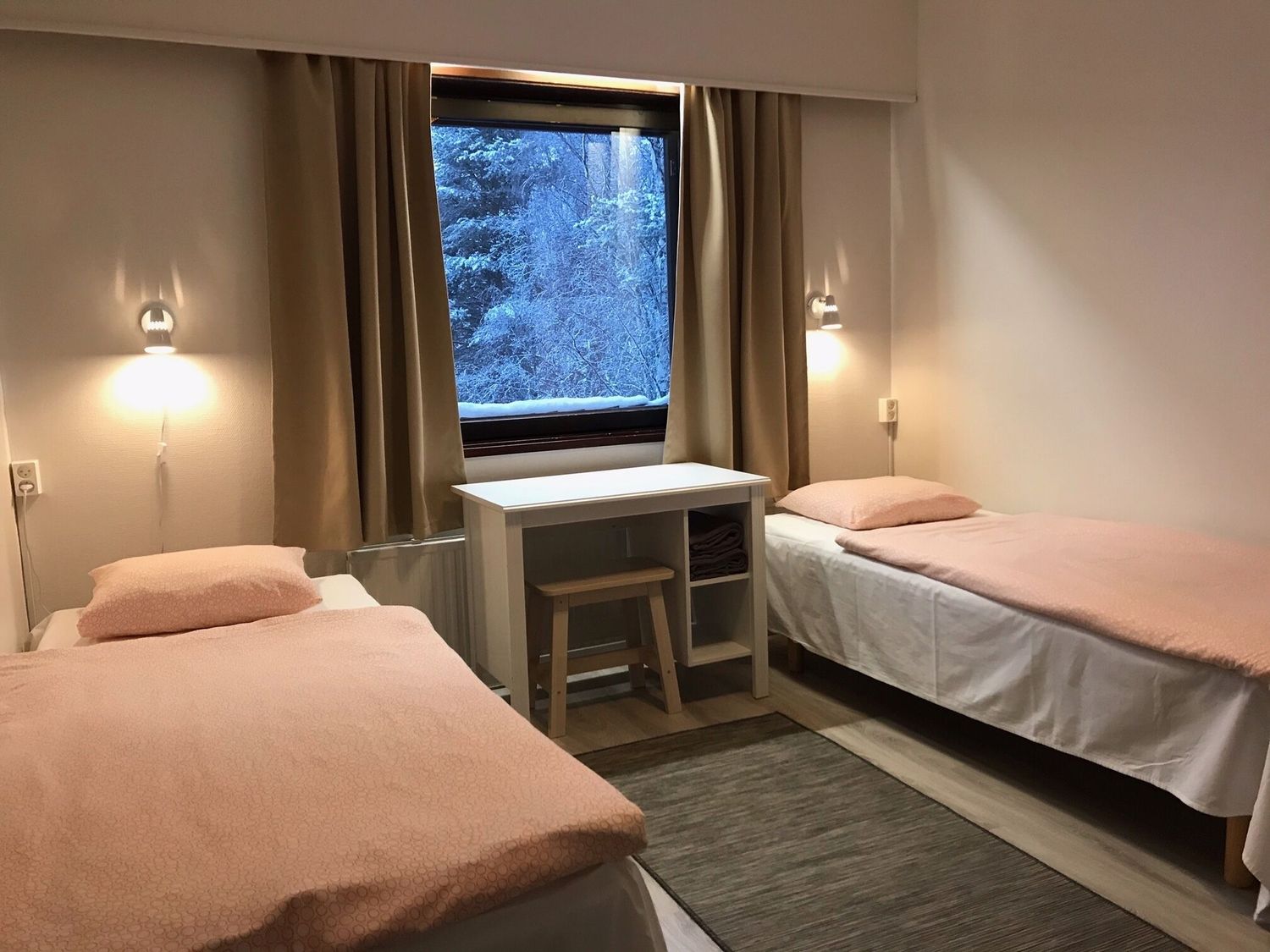 Modern hotel room interior with clean white bedding, wall sconces, and large windows offering natural light.