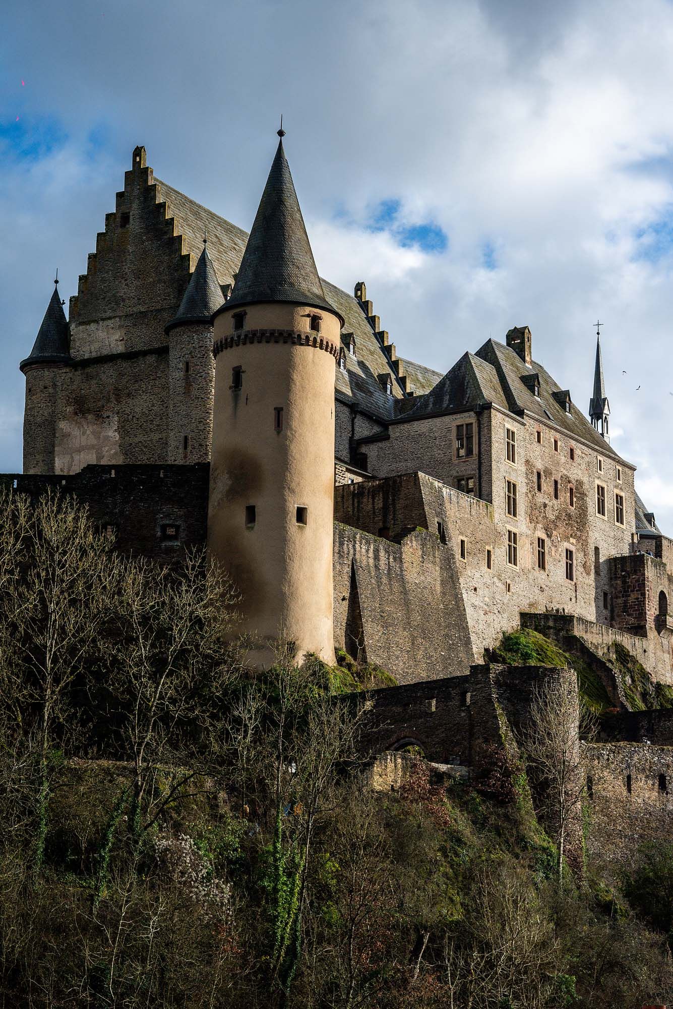 Medieval Vianden Castle perched on a hilltop in Luxembourg with dramatic stone towers and fortified walls against cloudy sky.