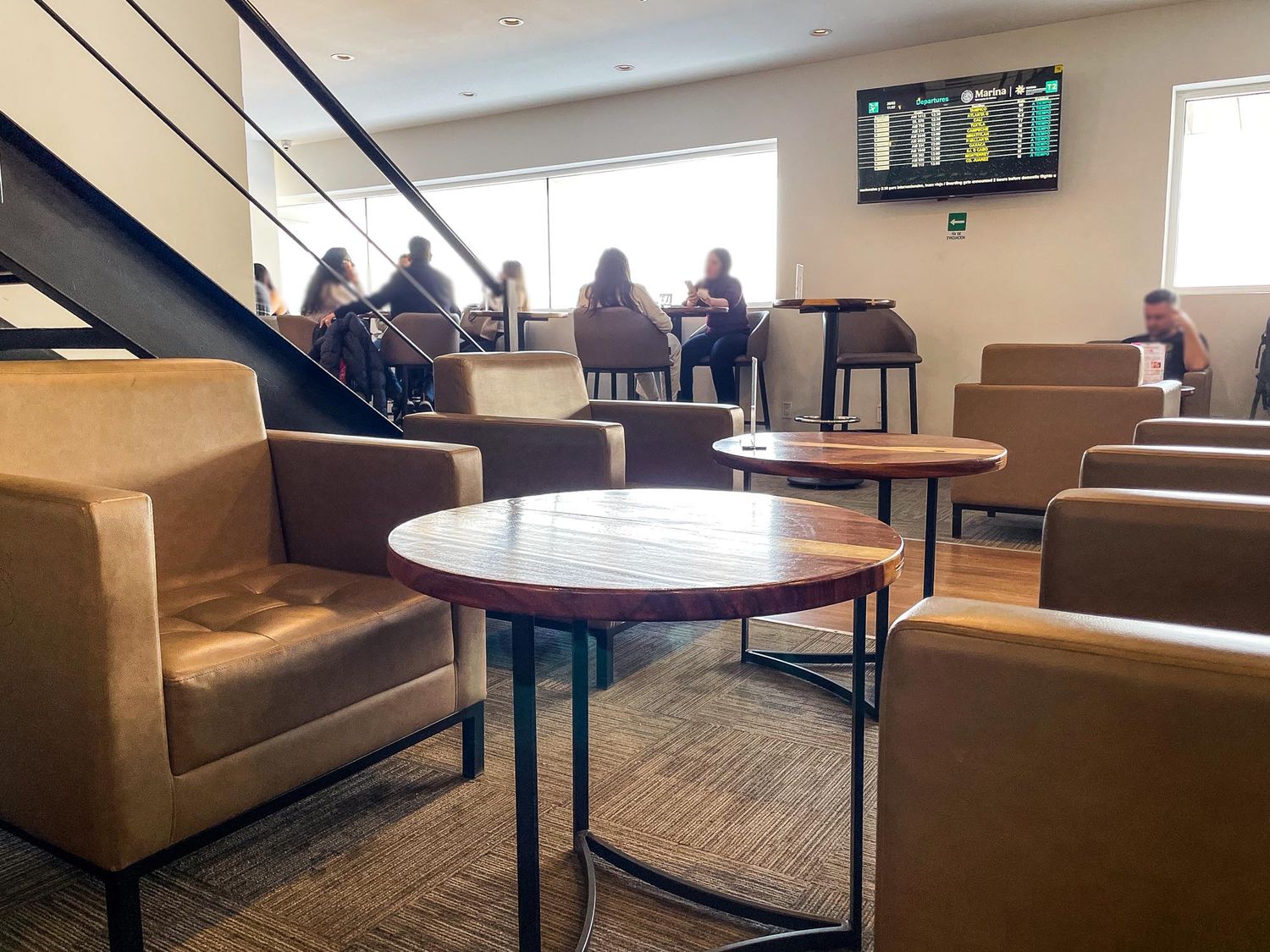 A modern lounge area with brown leather seating, round tables, and large windows creating a warm and inviting atmosphere.