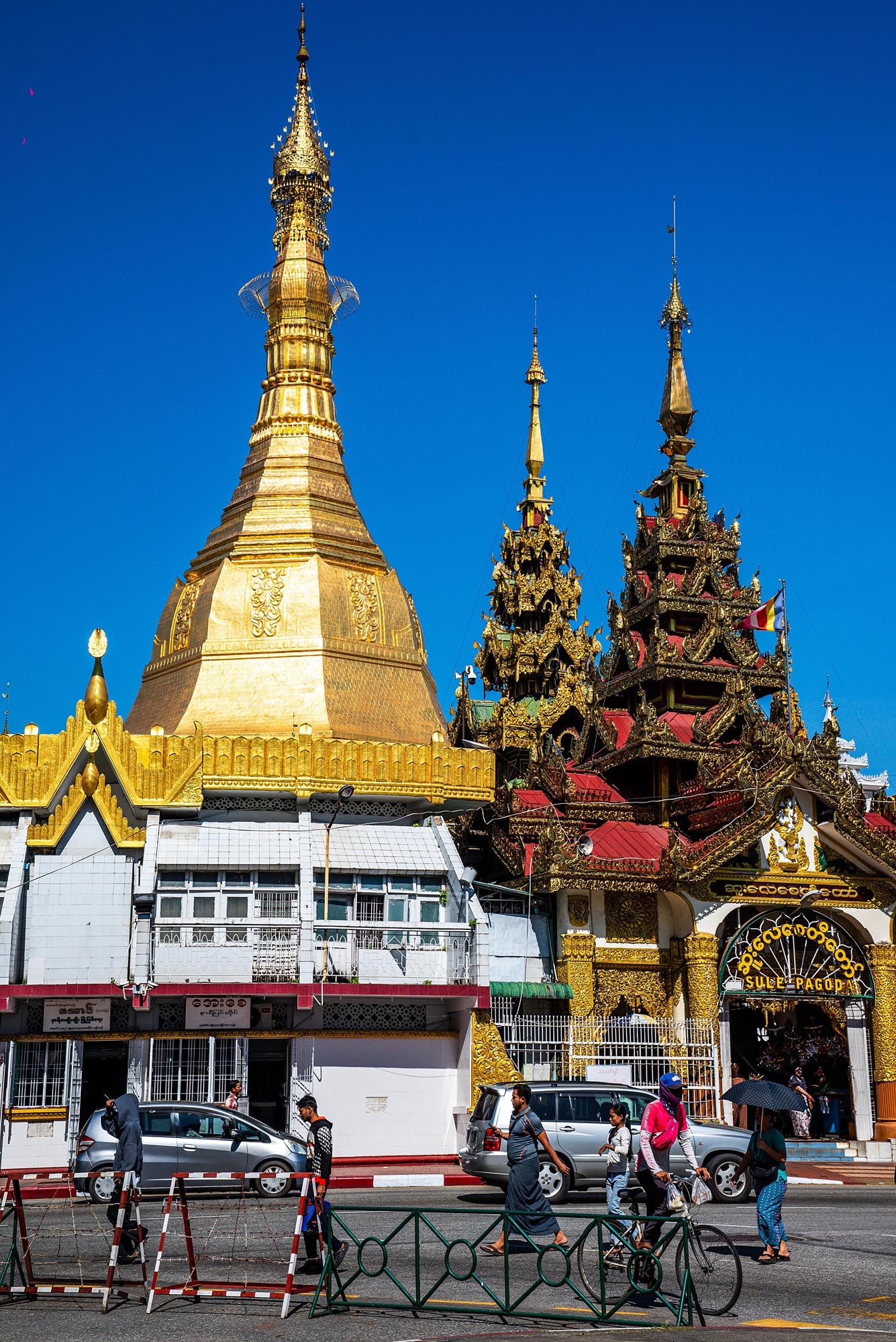 Golden Buddhist stupas and ornate temple architecture against bright blue sky in Myanmar.