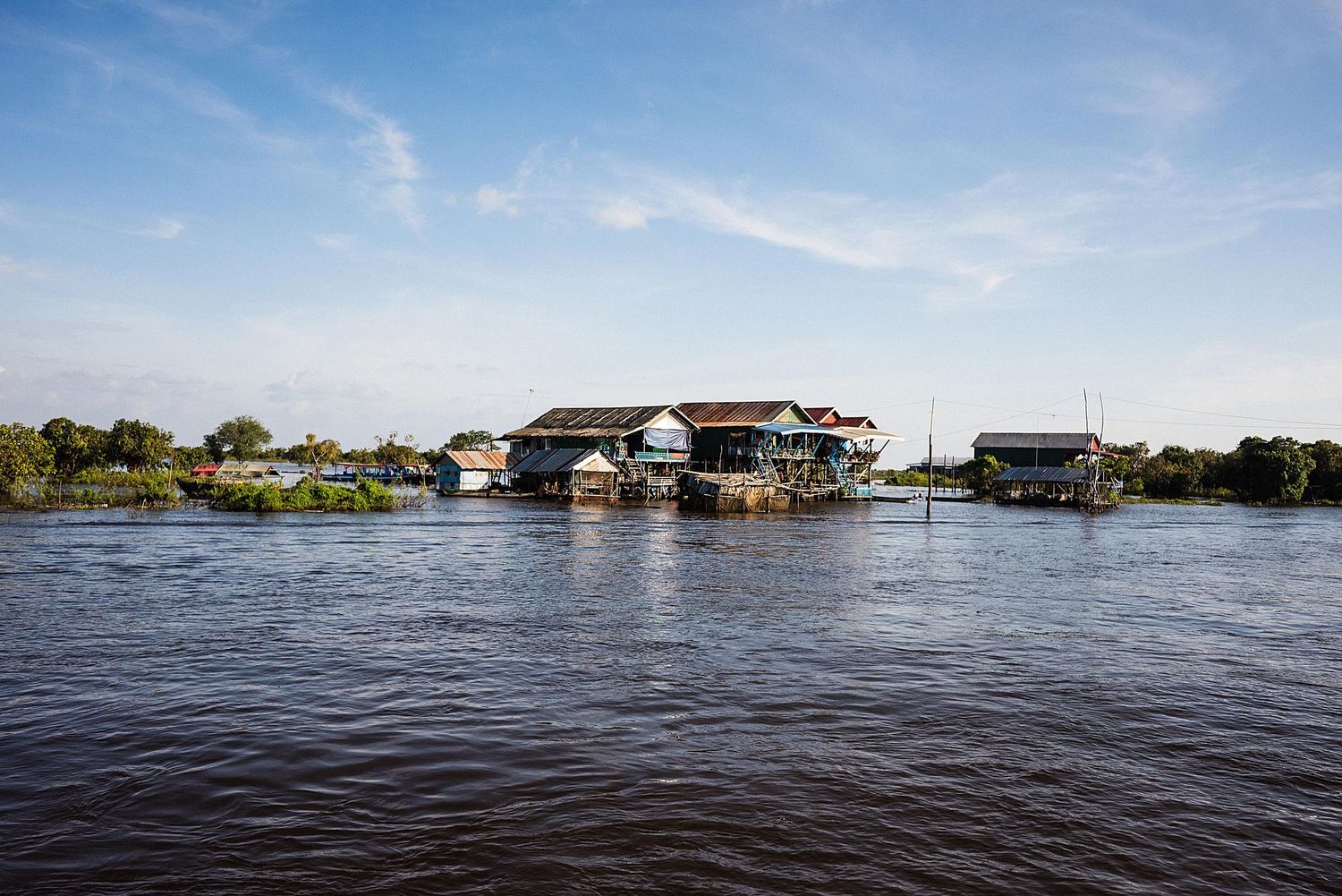 Panoramic view of a flooded residential area with homes surrounded by rising water under a blue sky.
