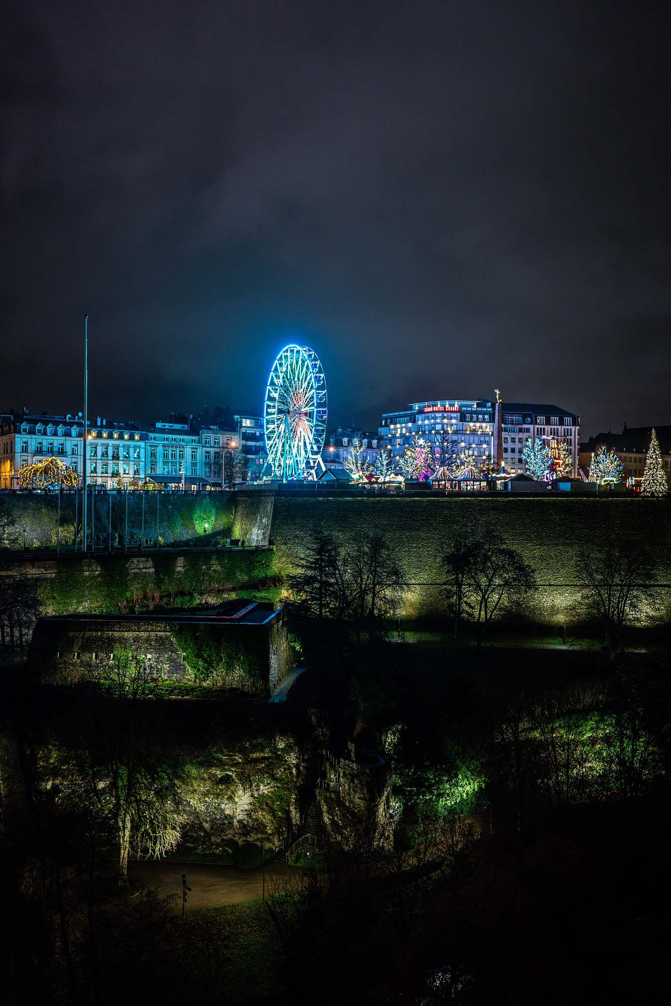 Illuminated nighttime cityscape with ferris wheel and buildings creating a colorful reflection against the dark sky.