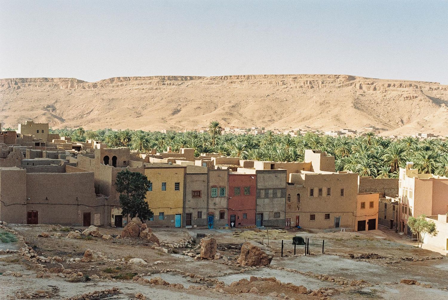 Panoramic view of traditional mud brick buildings and houses in a desert village with mountains in the background.