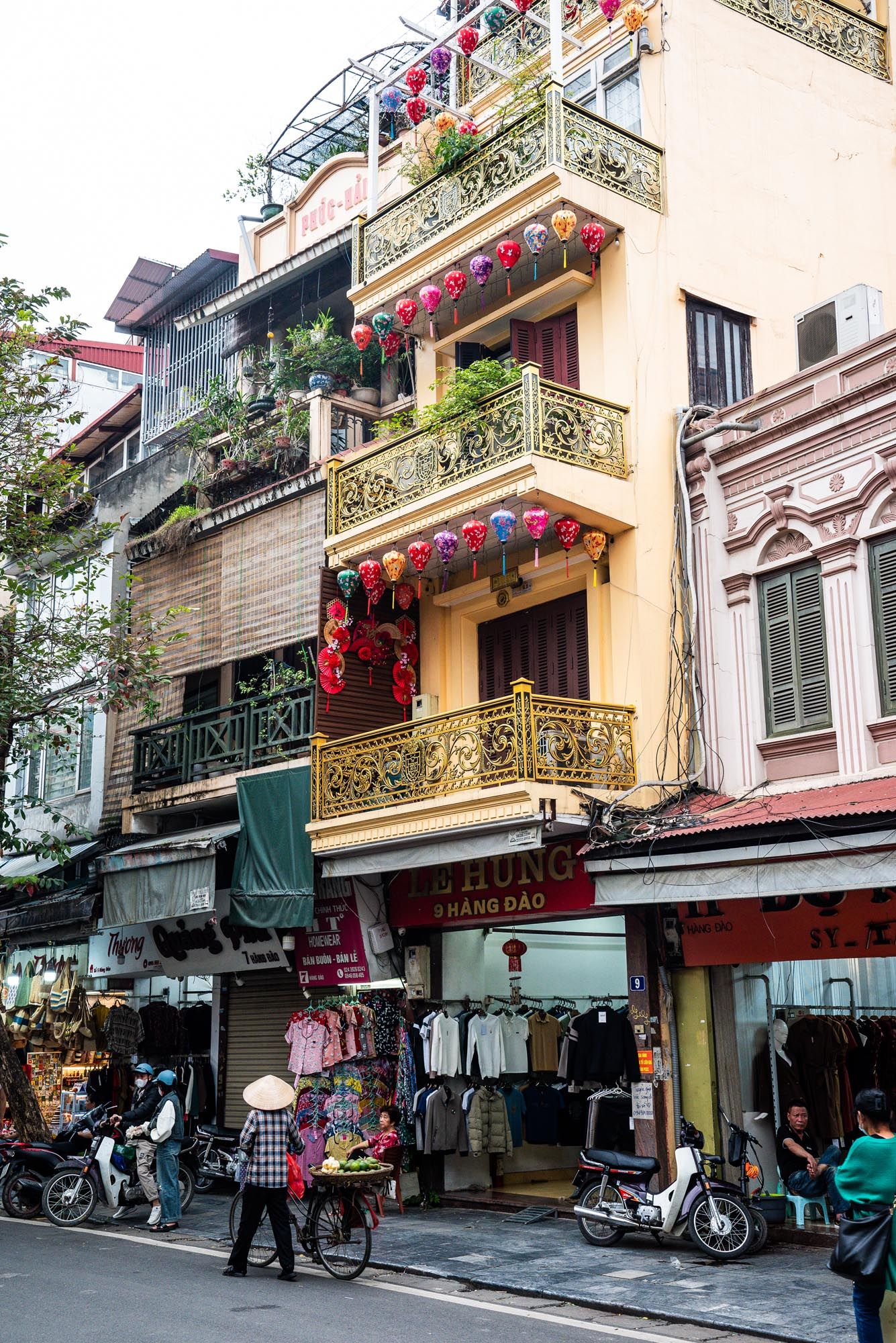 Colorful lanterns decorate balconies of traditional building above street vendors in Hanoi's Old Quarter, Vietnam.