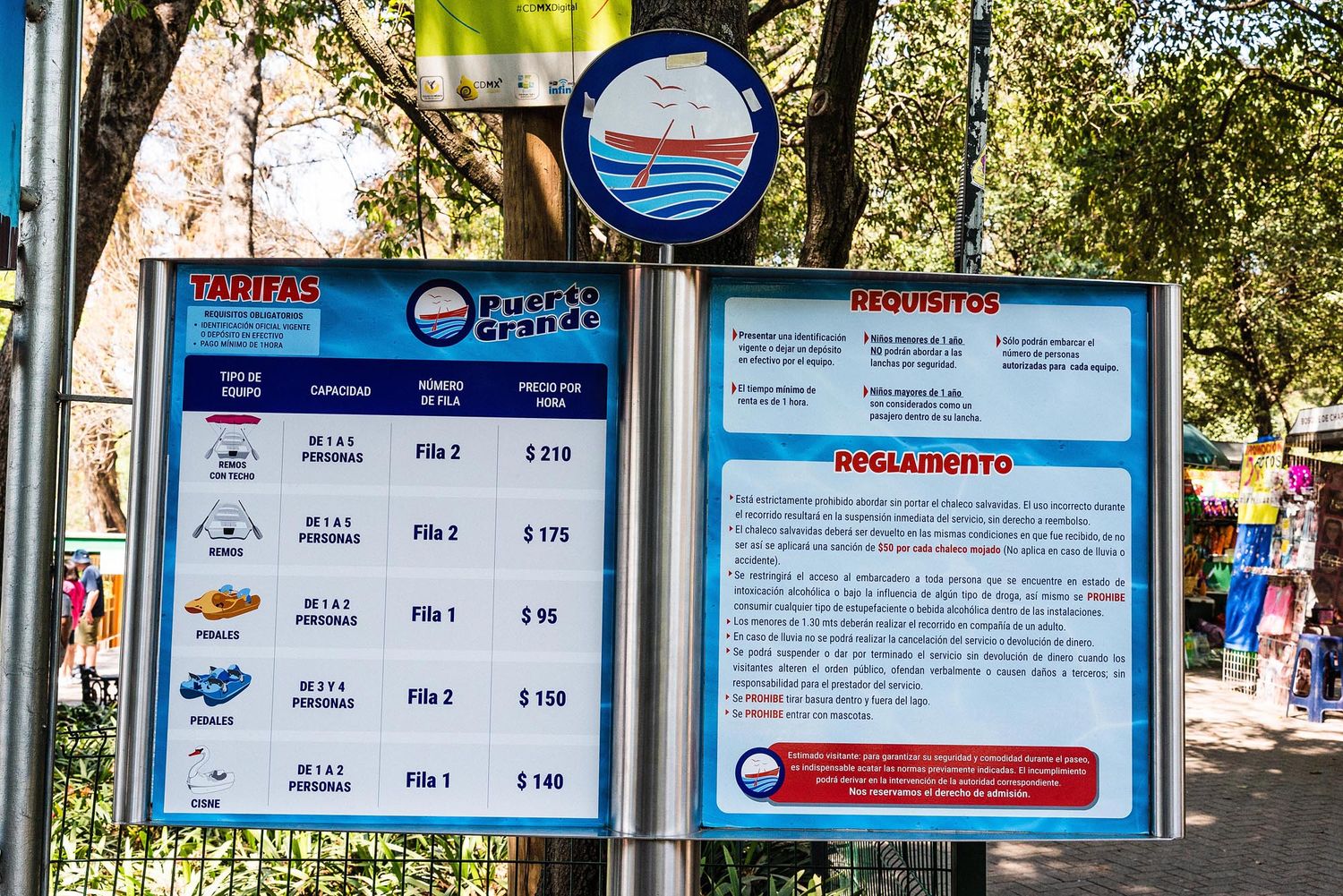 Blue and white pricing sign board displaying rates and regulations at an outdoor facility or park entrance.