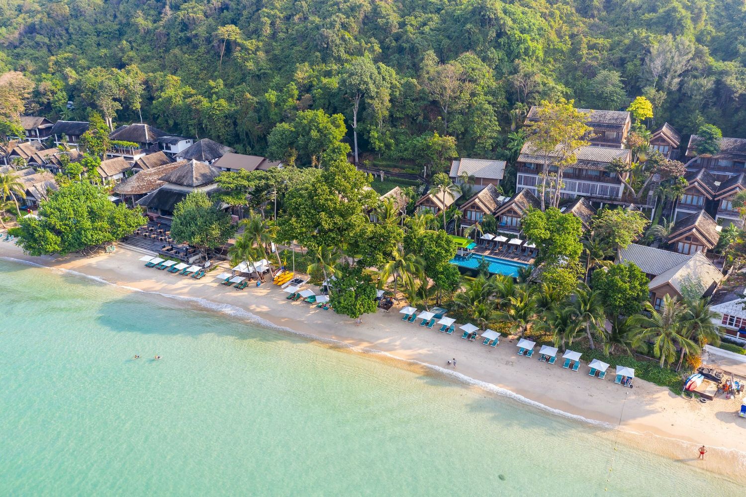 Aerial panoramic view of a tropical beachfront resort with turquoise waters, palm trees, and sandy coastline.