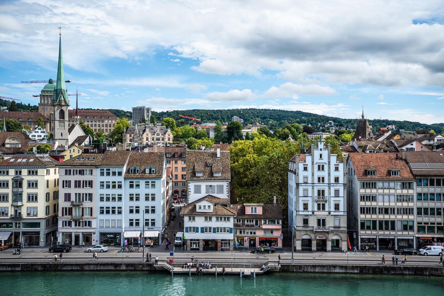 Panoramic view of historic white buildings along the waterfront in Zurich, Switzerland with mountains in the background.