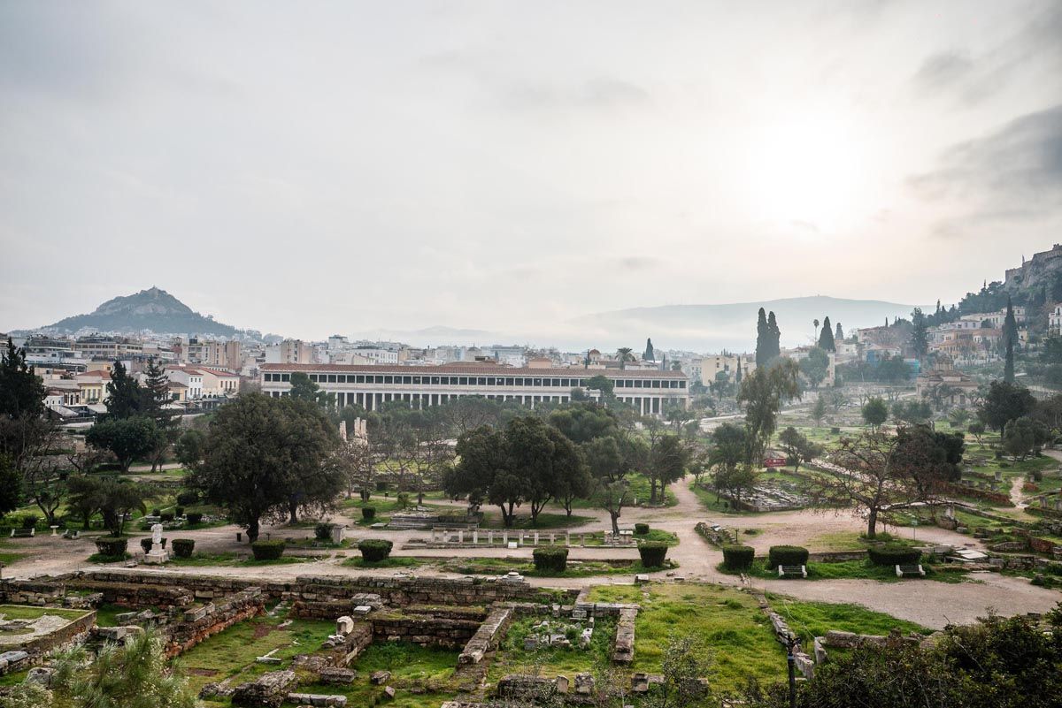 Ancient Agora archaeological site in Athens Greece with green grass and historic ruins under cloudy skies.