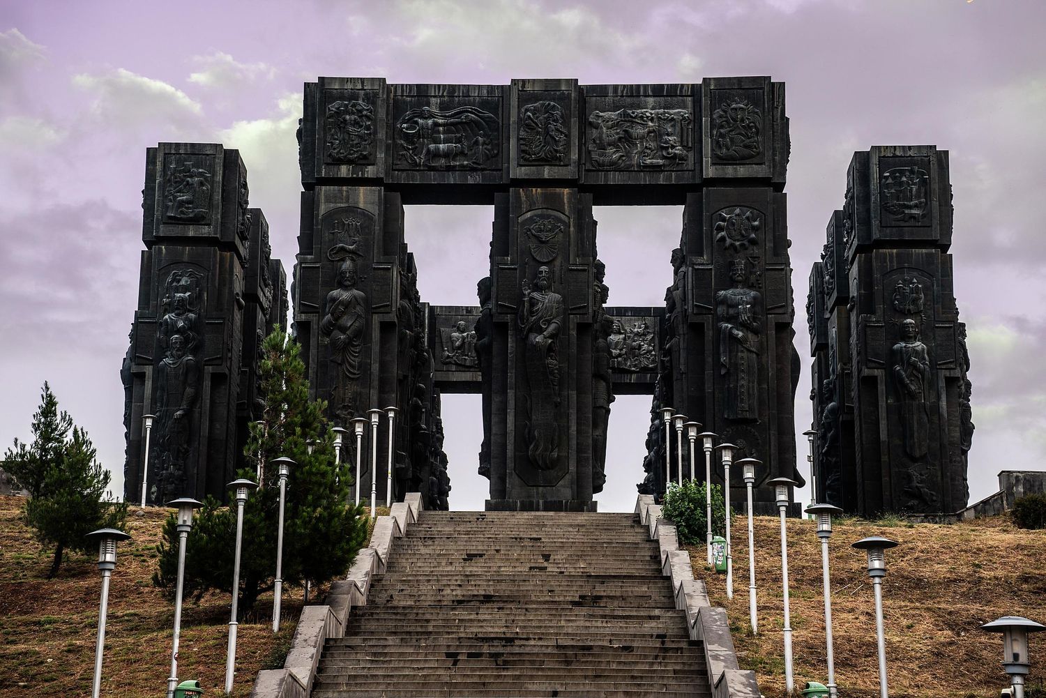 Ancient stone ruins stand against a moody purple sky with white flag poles in the foreground.