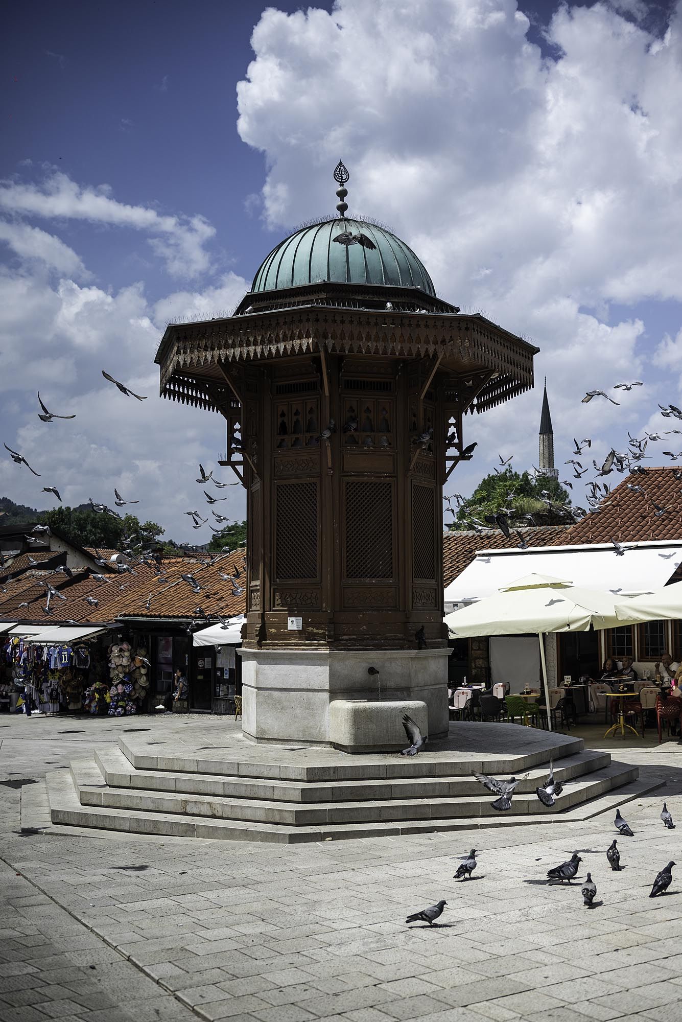 Historic gazebo in town square with pigeons gathering on stone steps under dramatic cloudy sky.