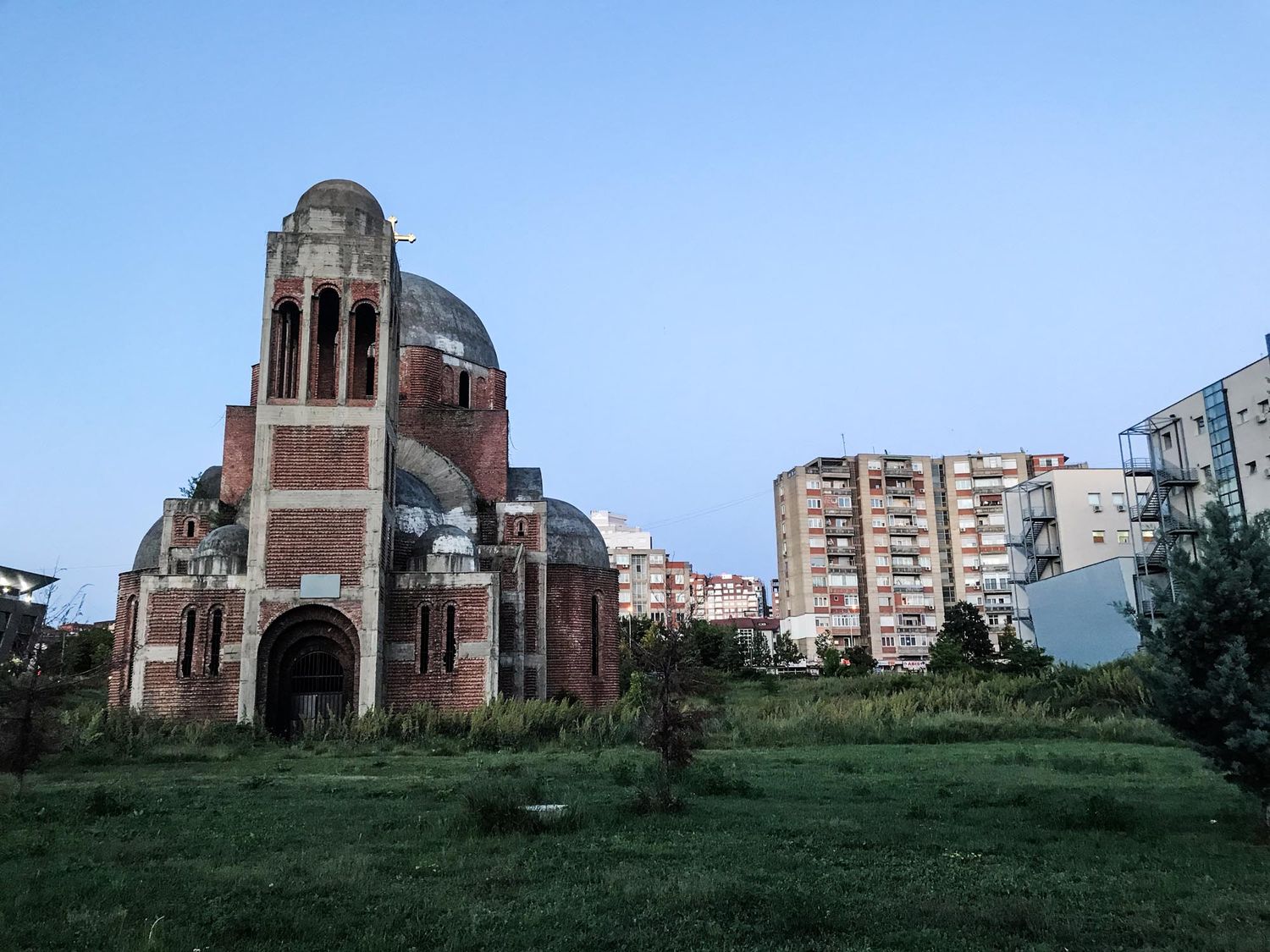 Panoramic view of an abandoned Orthodox church with red brick architecture set against a blue sky and green landscape.