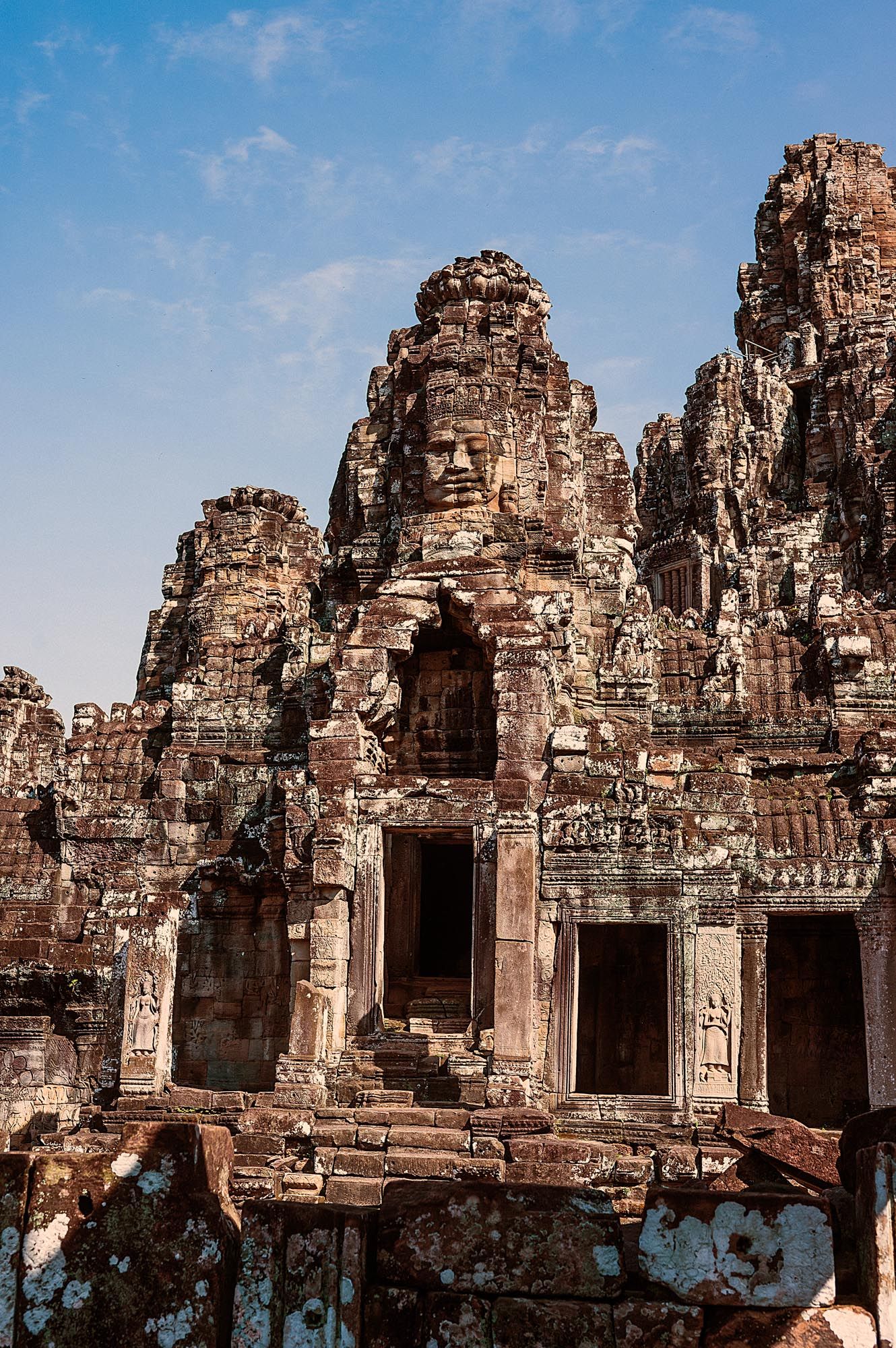 Ancient stone faces carved into the towers of Bayon Temple at Angkor Thom against blue sky in Cambodia.