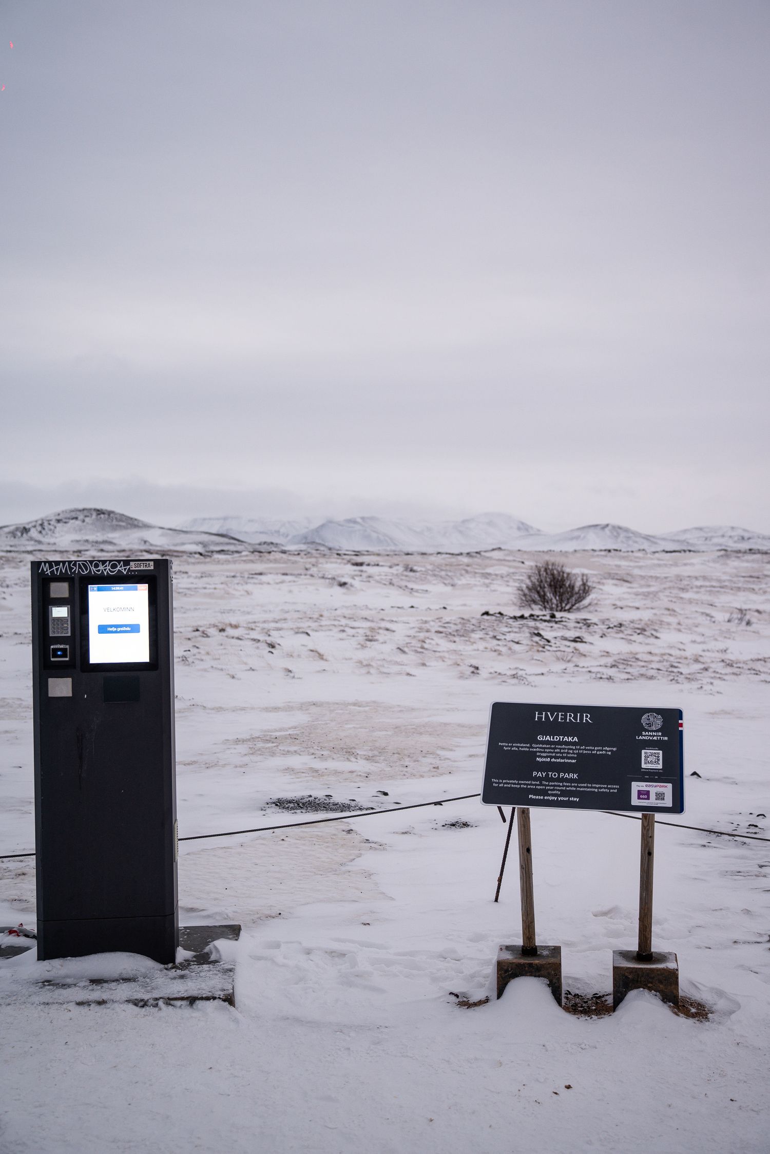 Lone payment terminal and information signs stand in a stark snowy winter landscape.