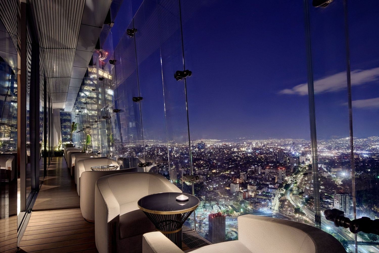 Panoramic view of a modern city skyline at night through floor-to-ceiling windows in a luxury high-rise apartment.