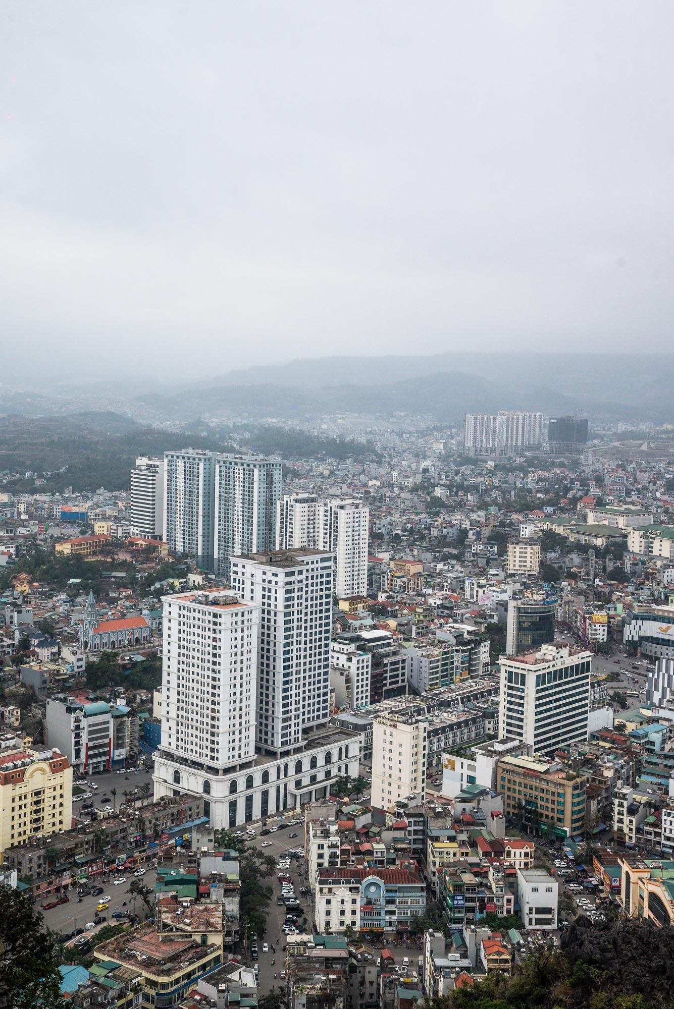 Aerial cityscape view of modern high-rise buildings and residential neighborhoods in a foggy urban setting with mountains.