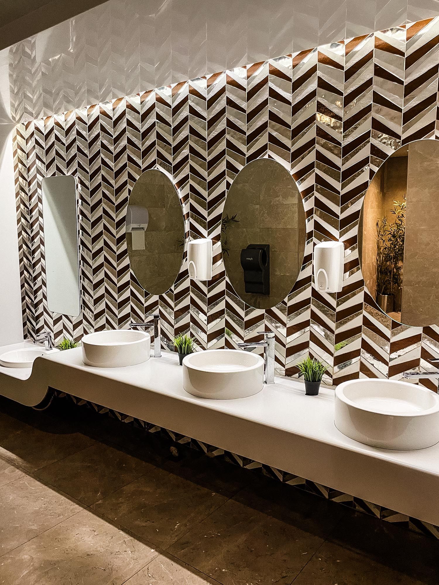 Modern bathroom interior with chevron patterned tile wall, round mirrors, and white vessel sinks on floating counter.