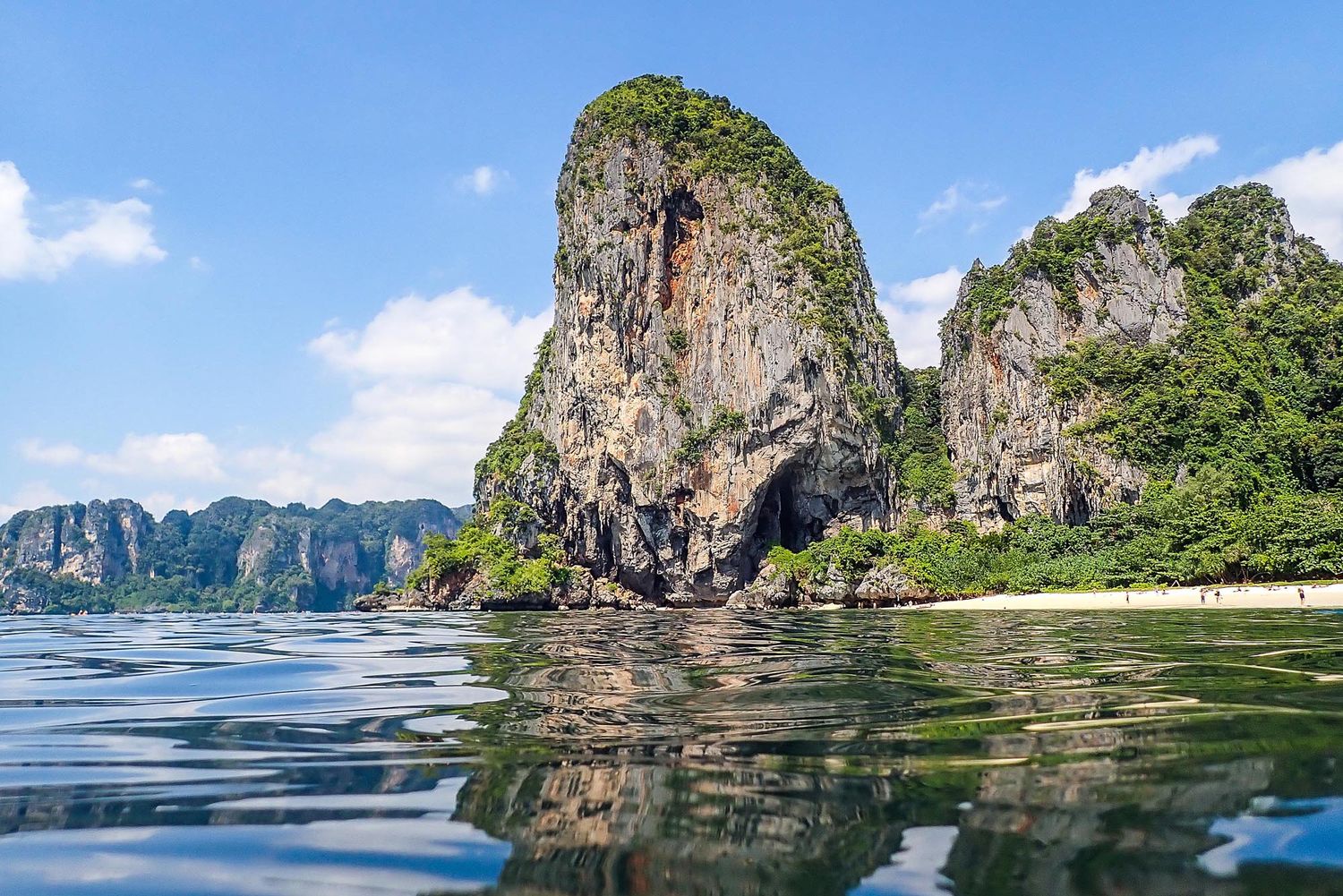 Scenic limestone cliffs rise dramatically from turquoise waters along a tropical coastline in Thailand.