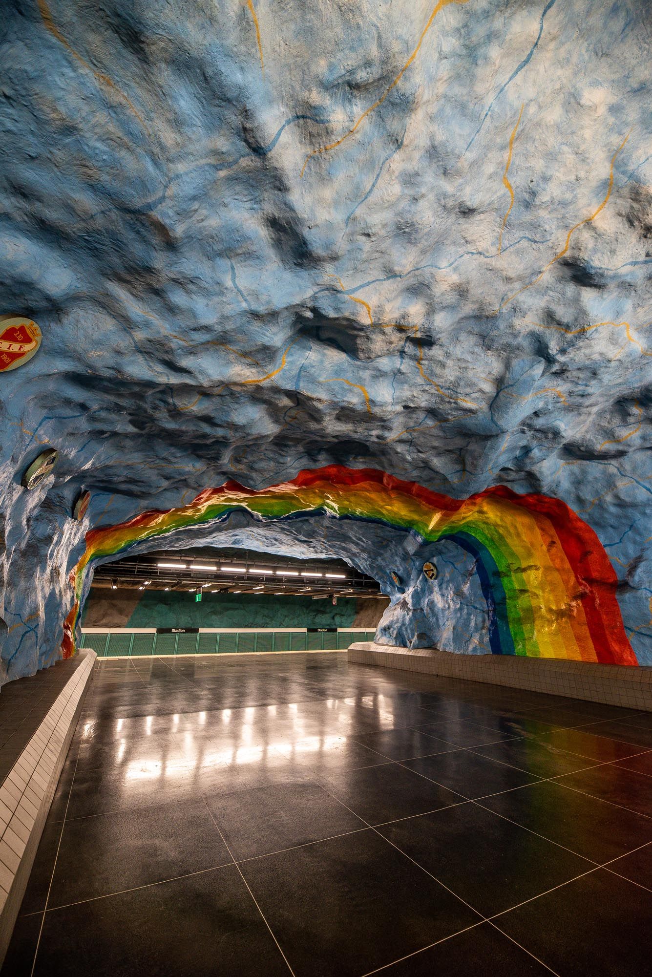 Stockholm subway station features a dramatic cave-like interior with rough stone walls and vibrant rainbow art installation.