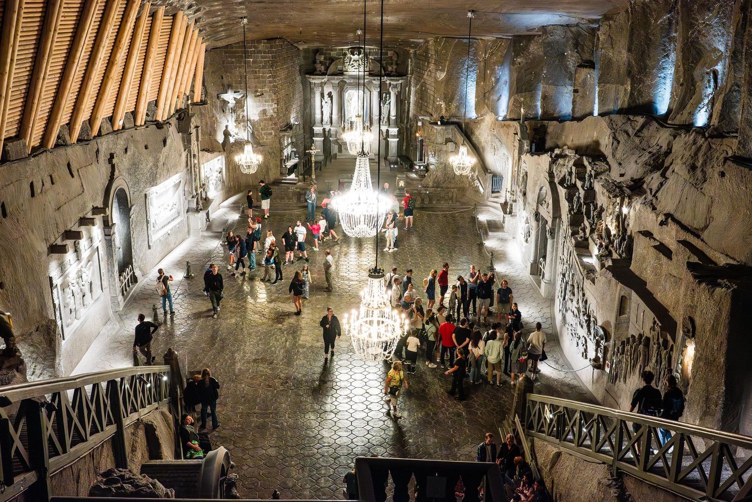 Historic interior of the Wieliczka Salt Mine in Poland with ornate chandeliers illuminating a vast underground chamber.