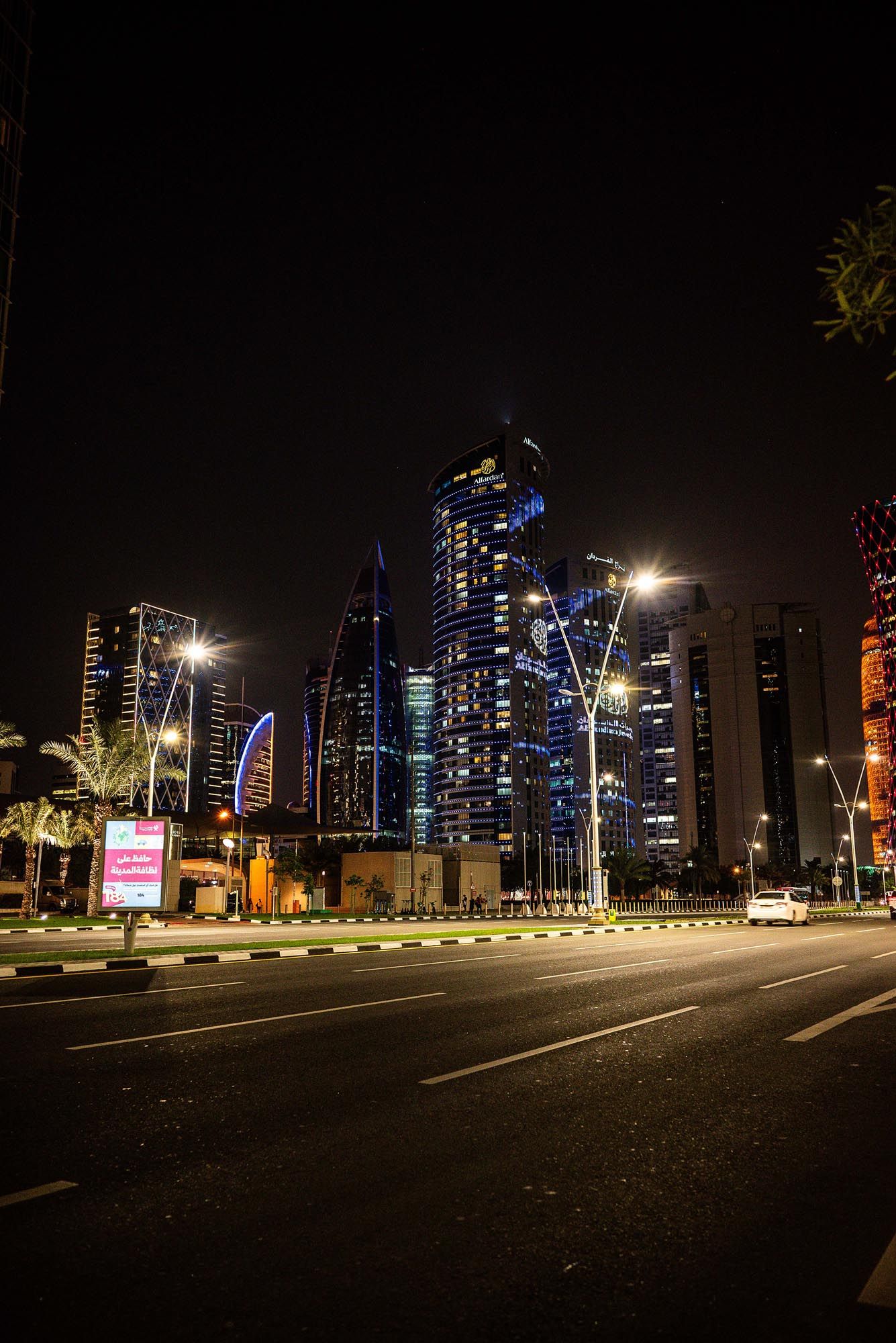 Modern city skyline of Doha, Qatar illuminated at night with skyscrapers and empty streets.