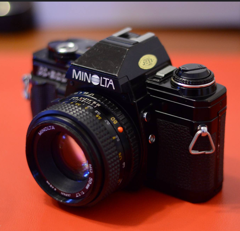 Vintage black Minolta SLR film camera with 50mm lens on orange background.