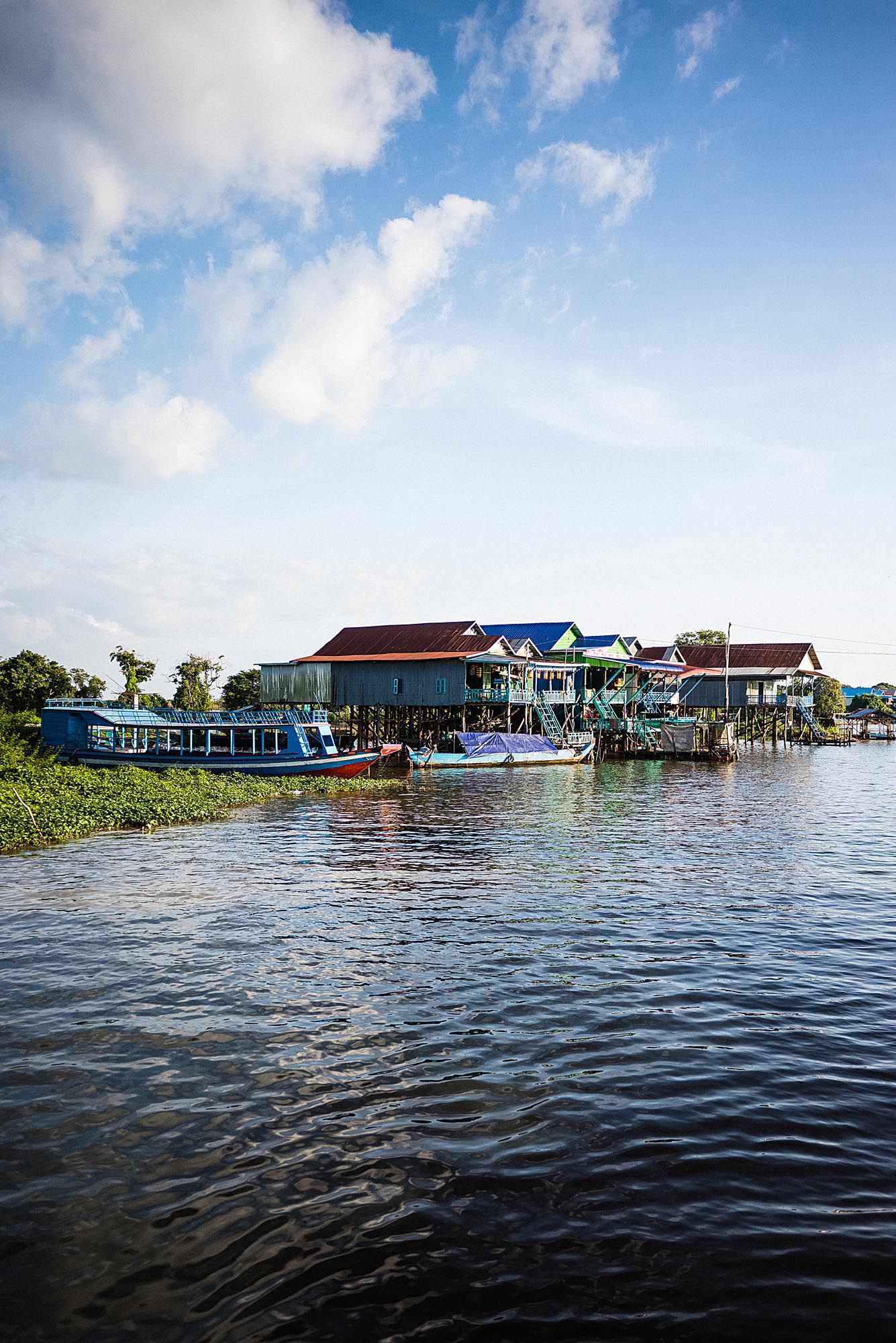 Panoramic view of colorful floating houses and boat docks on a calm lake under bright blue sky with white clouds.
