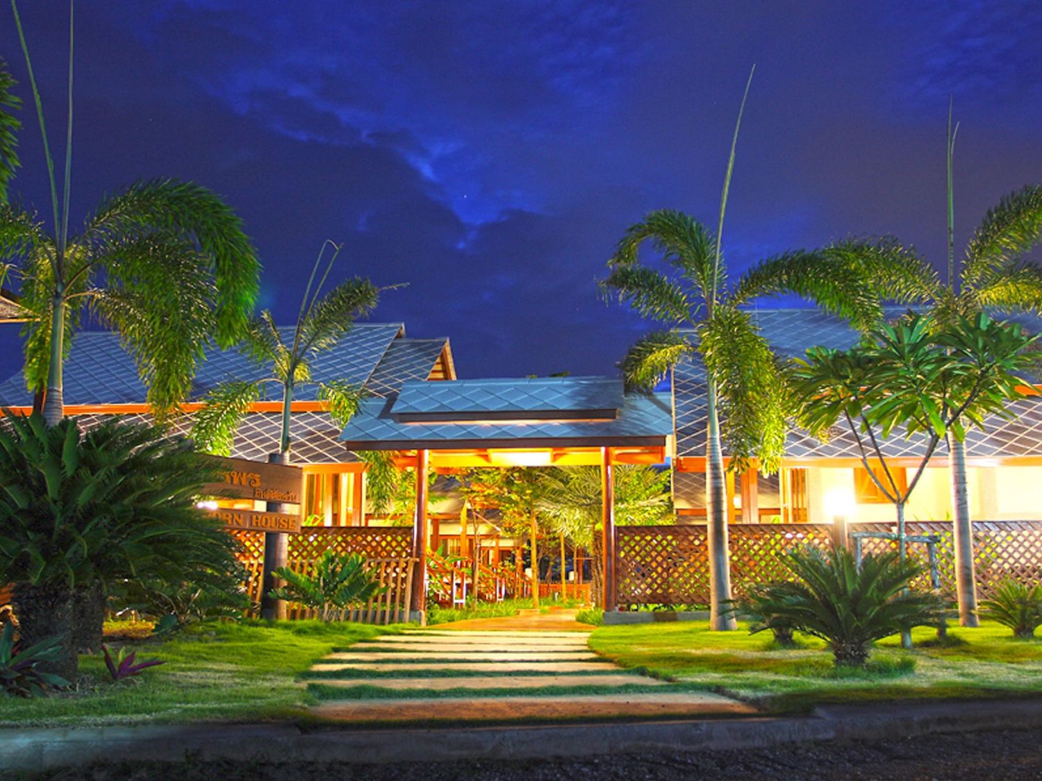 Panoramic view of a tropical resort illuminated at night with palm trees and buildings under a deep blue sky.