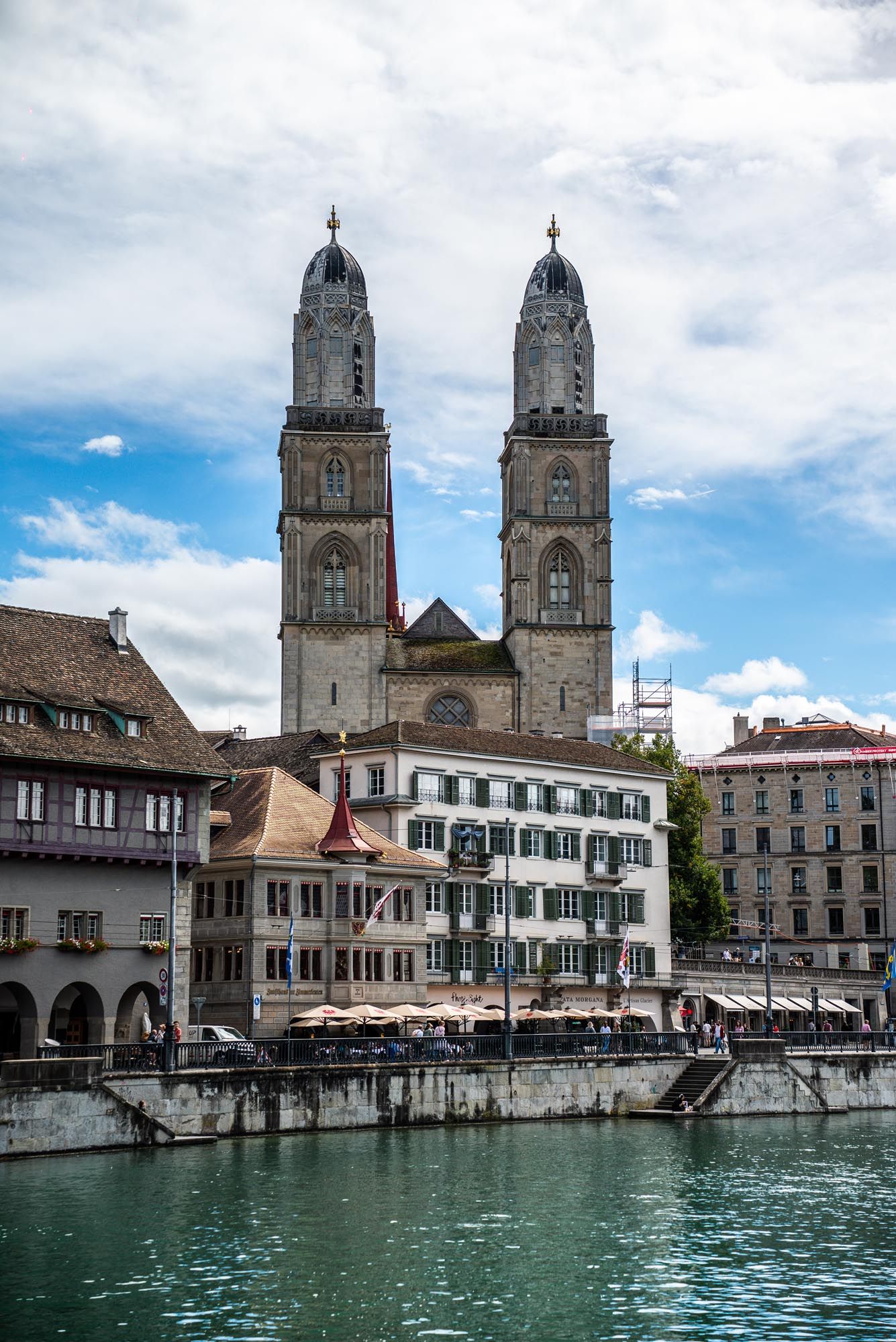 Historic Grossmunster cathedral with twin towers stands along the Limmat River waterfront in Zurich, Switzerland.