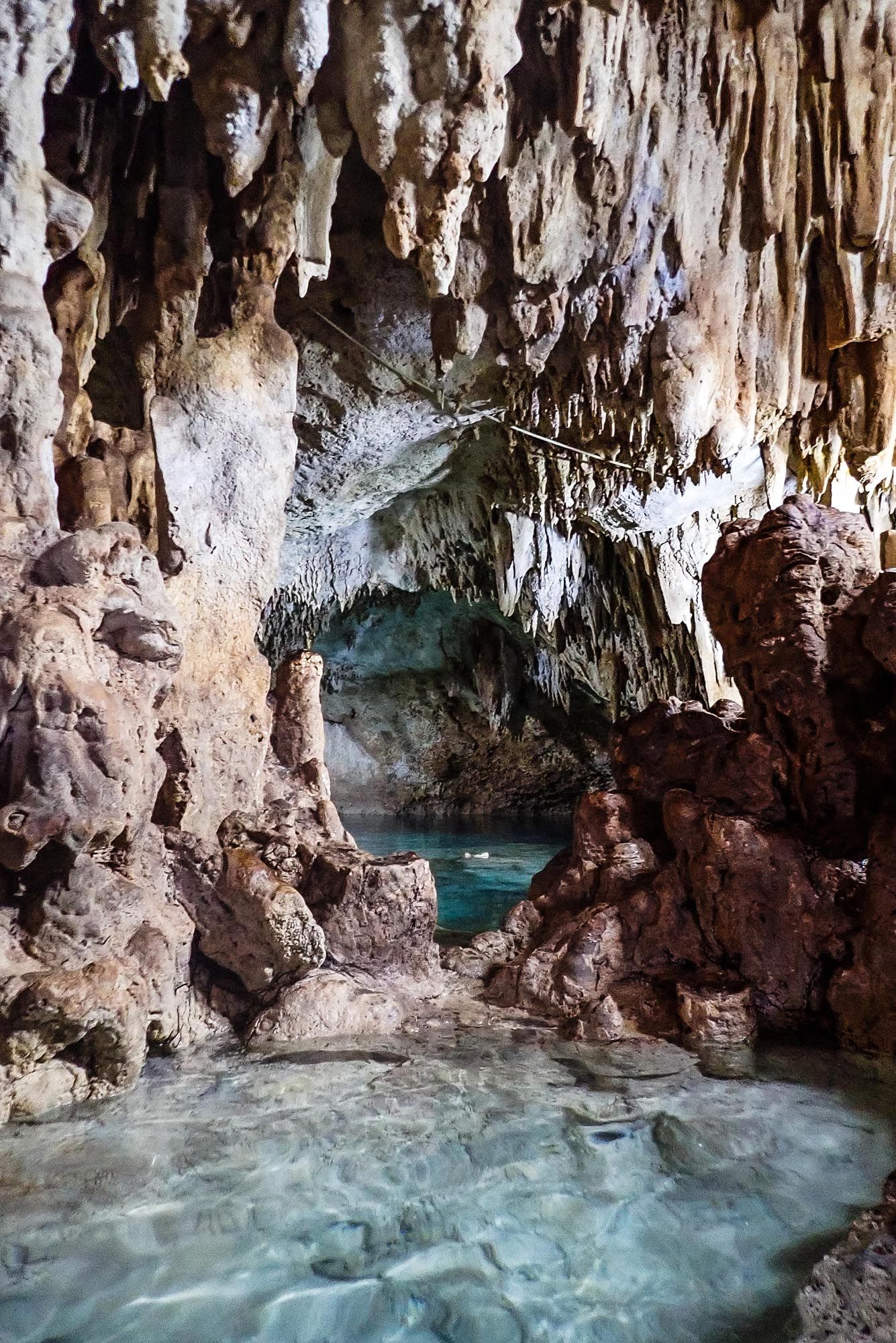 Stunning limestone cave formations hang above crystal clear turquoise waters in an underground cavern system.