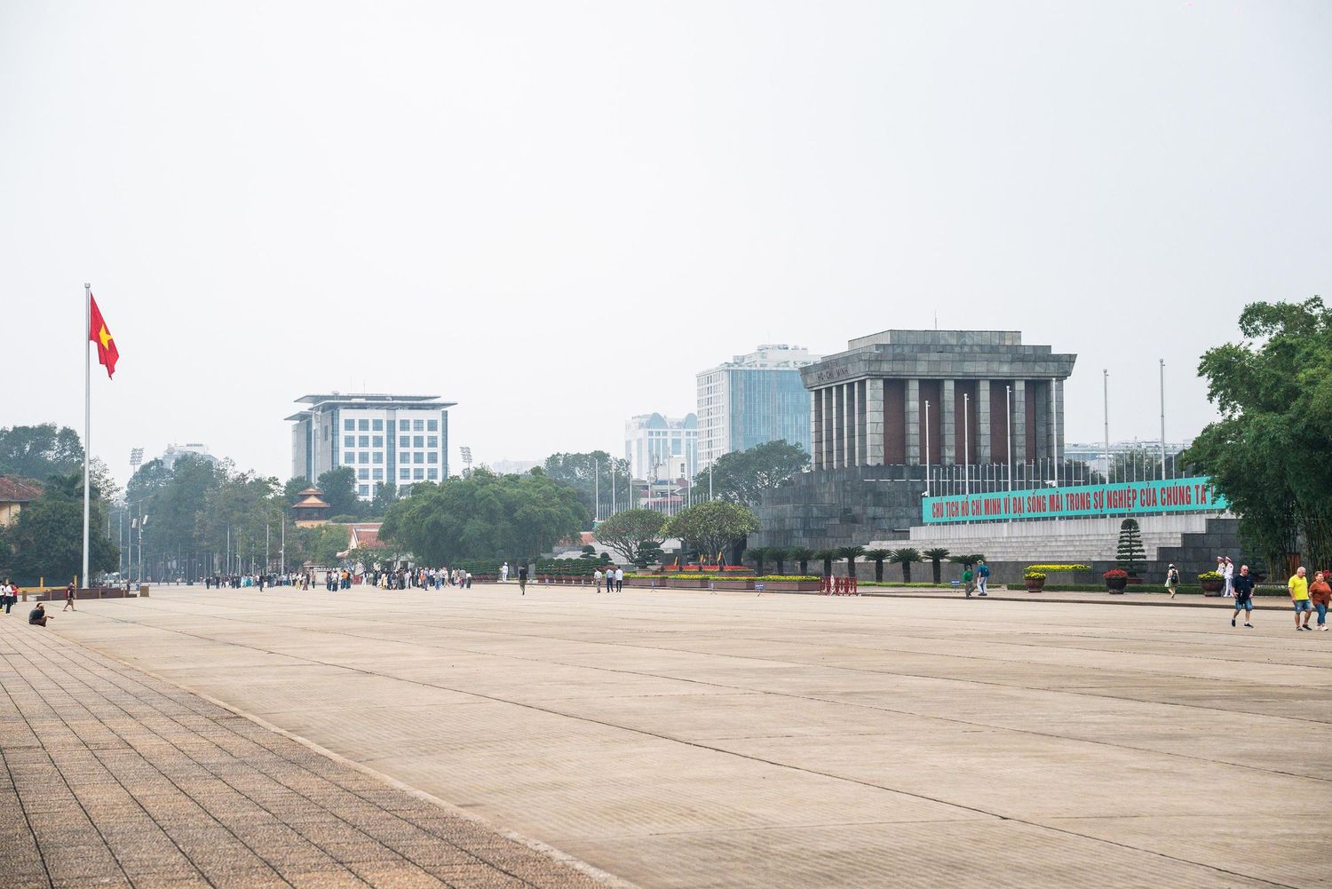Large paved square with historic memorial building in Hanoi, Vietnam on a misty day with red flag flying above.