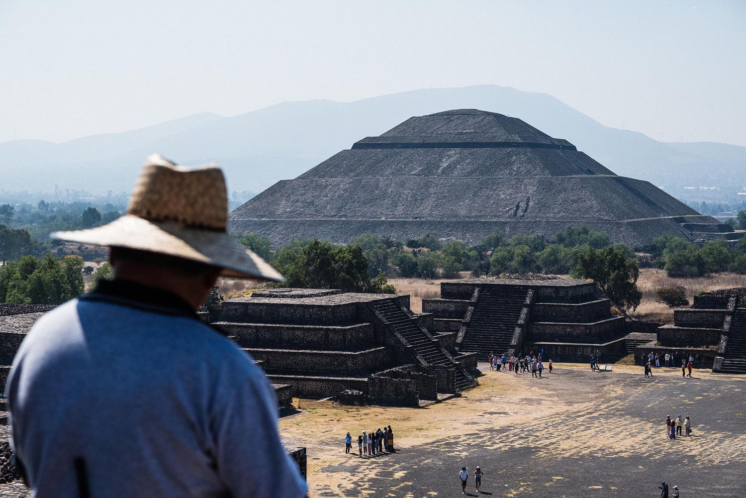 A tourist overlooks the ancient Pyramid of the Sun at Teotihuacan archaeological site in Mexico with mountains in background.