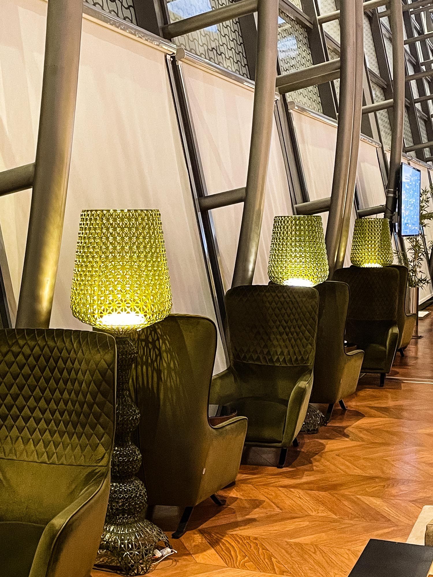 Modern lounge area with high-backed velvet chairs and herringbone wood flooring illuminated by warm accent lighting.