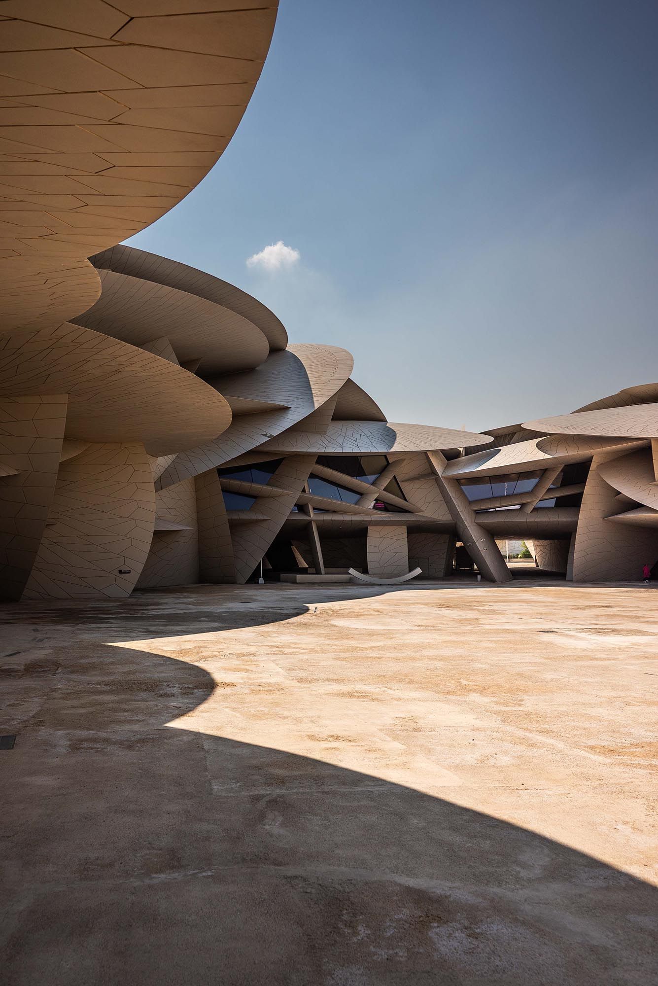 Curved concrete architecture of the National Museum of Qatar features dramatic angular walls under bright blue sky.